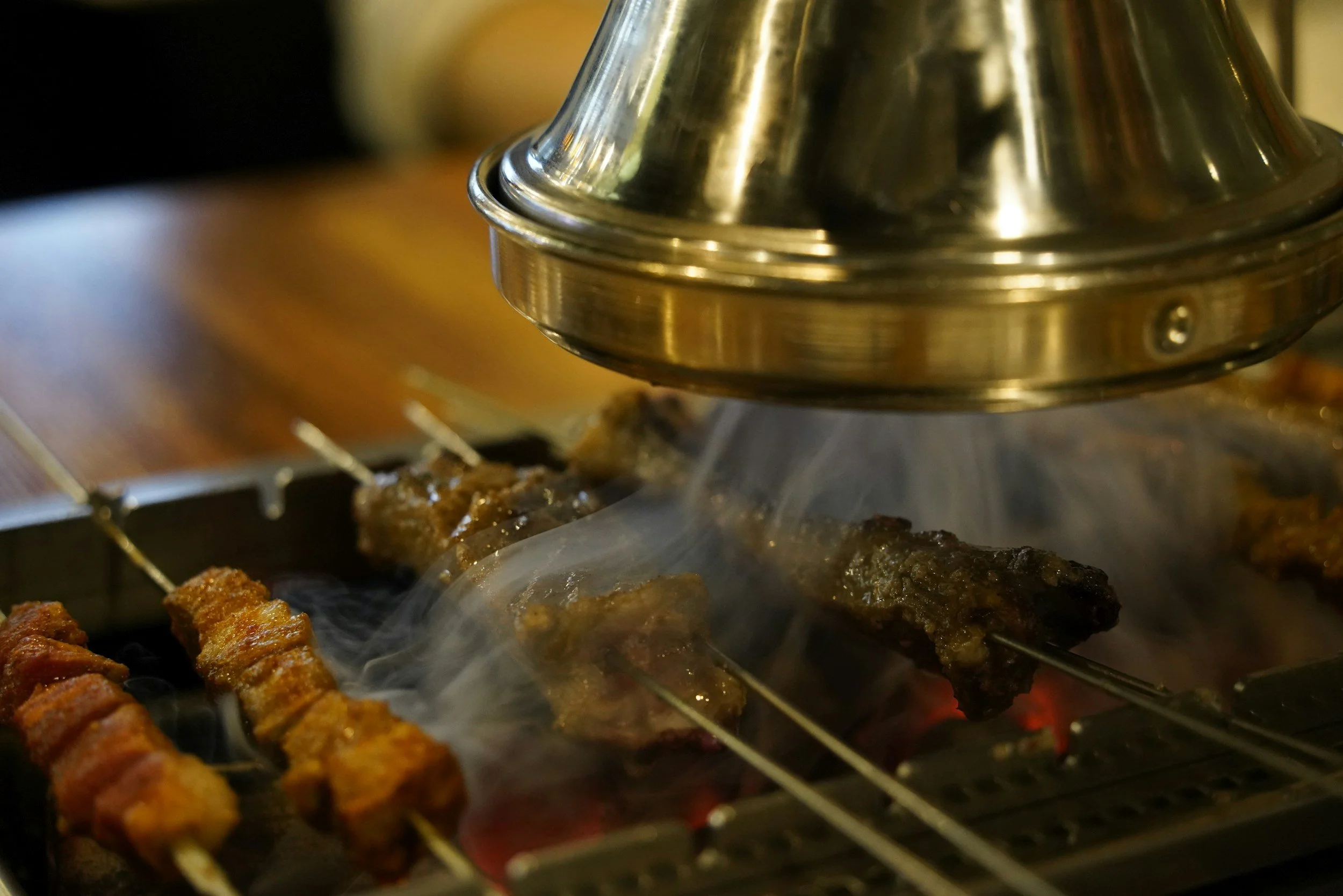 Close-up of skewers of meat grilling inside an oven with a metal baking rack above the flames.