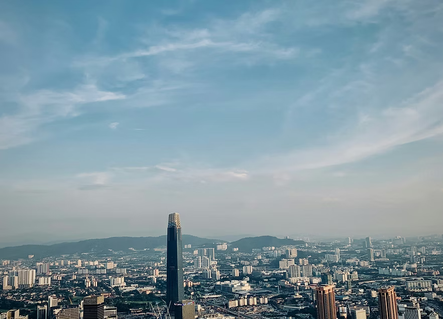 A city skyline with a prominent tall, dark skyscraper and a clear blue sky with scattered clouds.