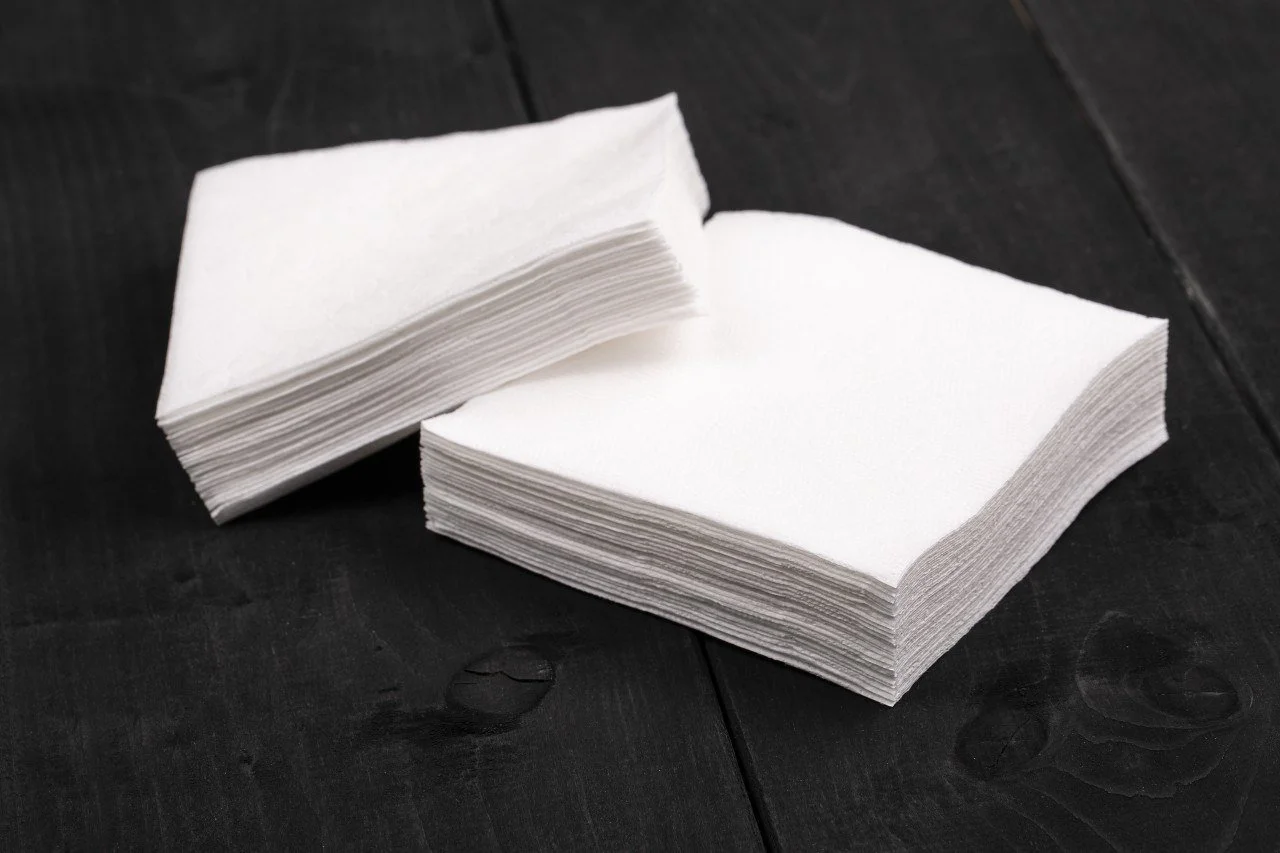 Two stacks of white paper napkins on a dark wooden surface.