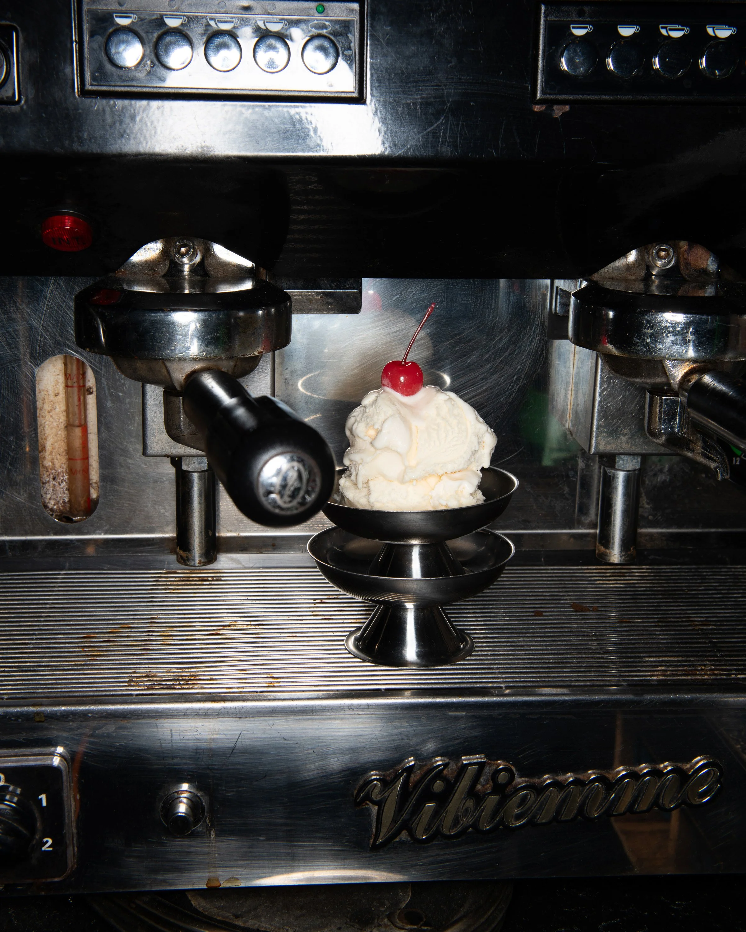 Une machine à café en métal avec une glace à la vanille et une cerise rouge dessus, positionnée au centre de la machine.