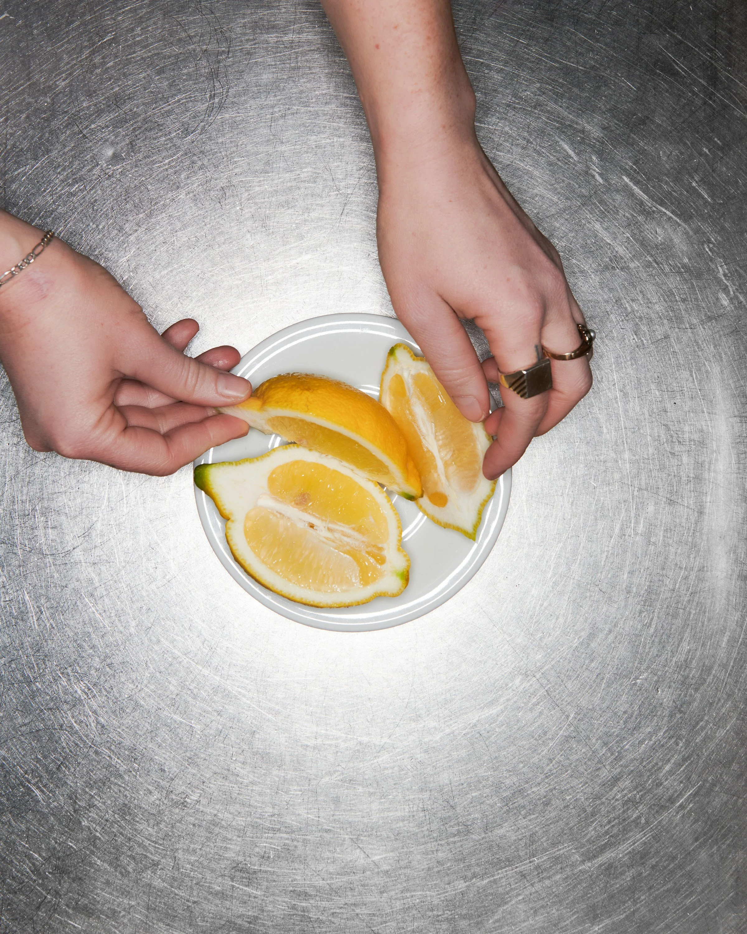 Mains tenant des quartiers d'agrumes, dont un citron et une orange, sur une assiette blanche en acier inoxydable.