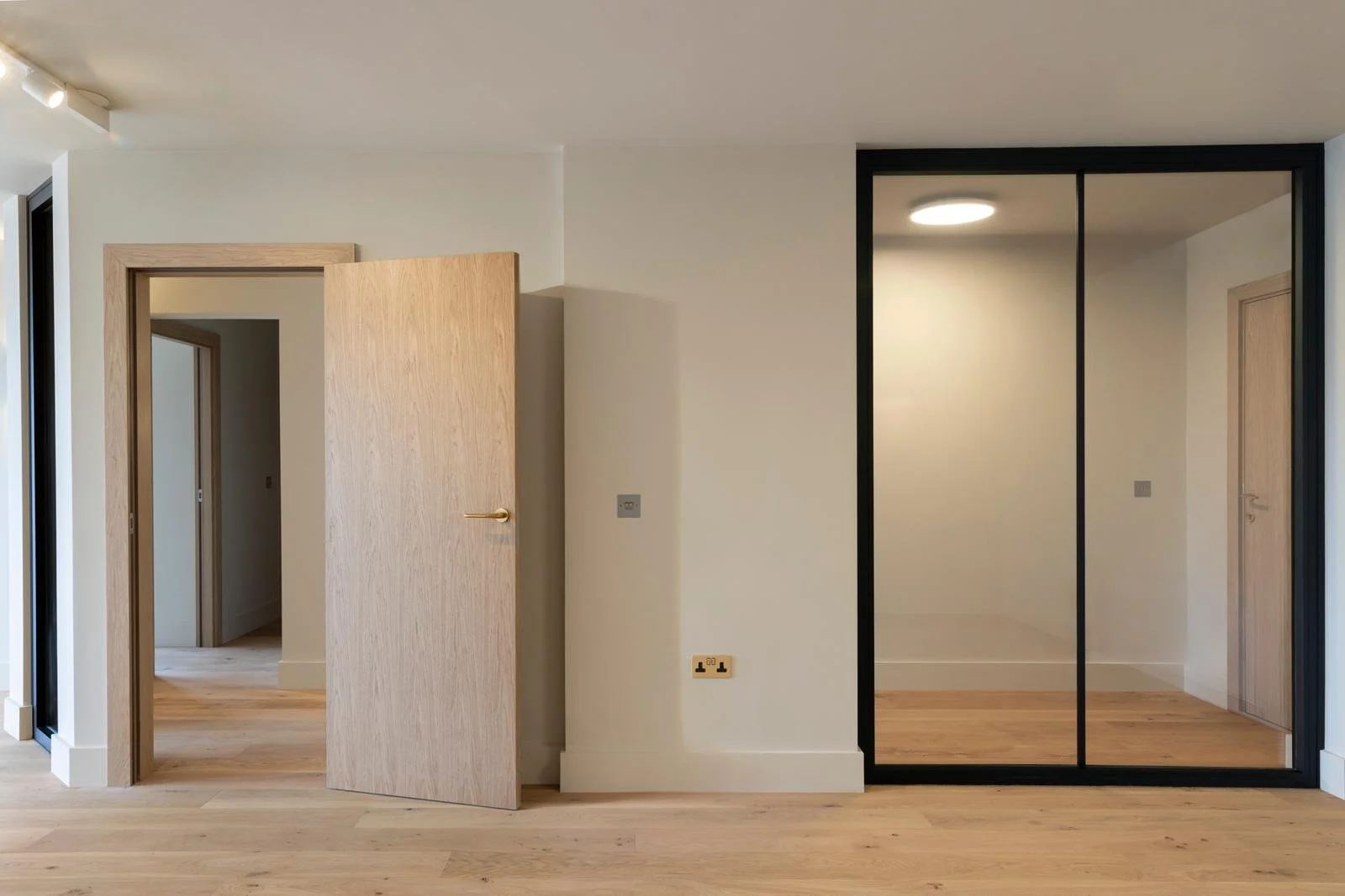 Empty room with wooden flooring, open wooden door, and sliding glass closet doors.