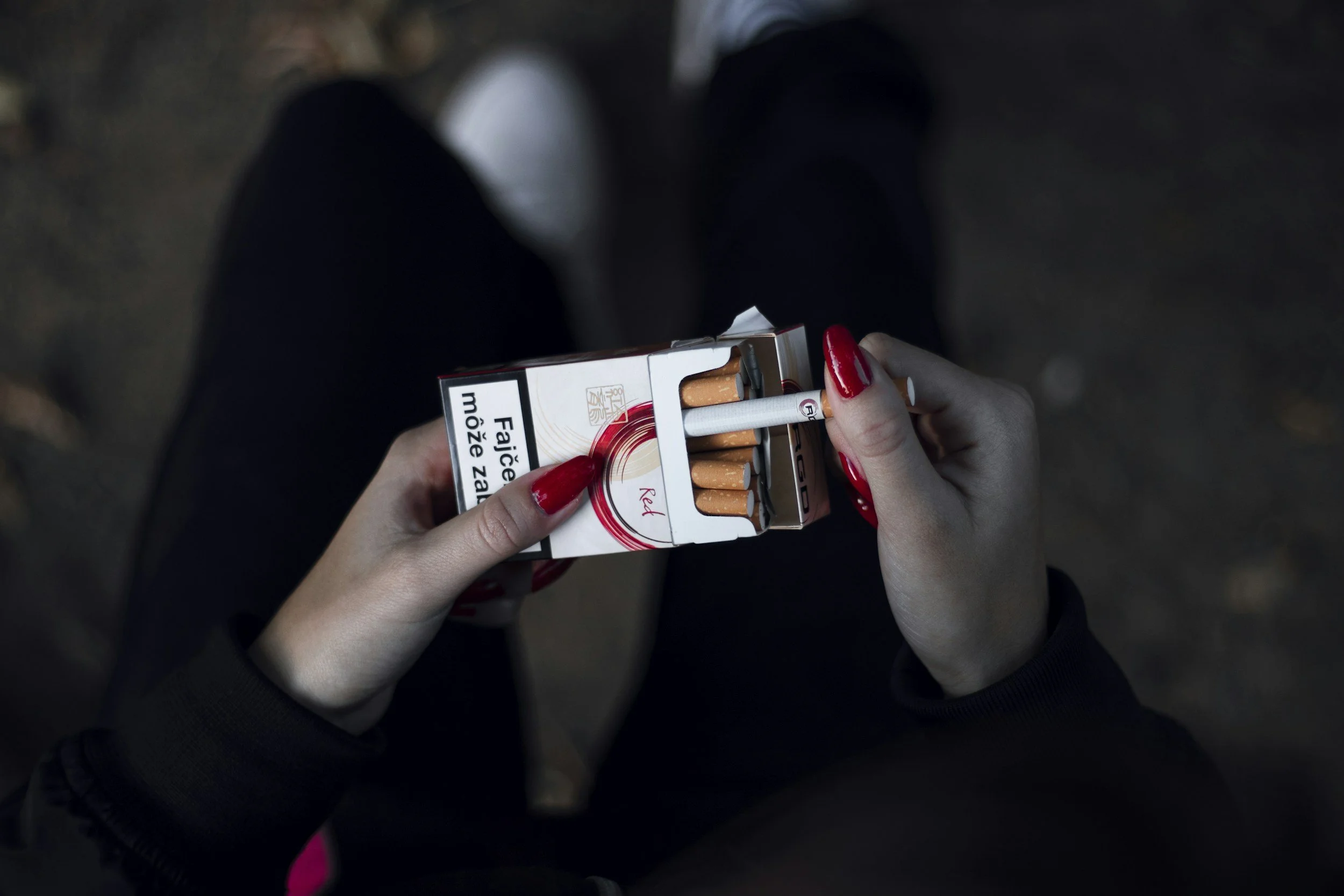 woman reaching for cigarette out of a packet illustrating the daily ritual and relationship with smoking that lingers.