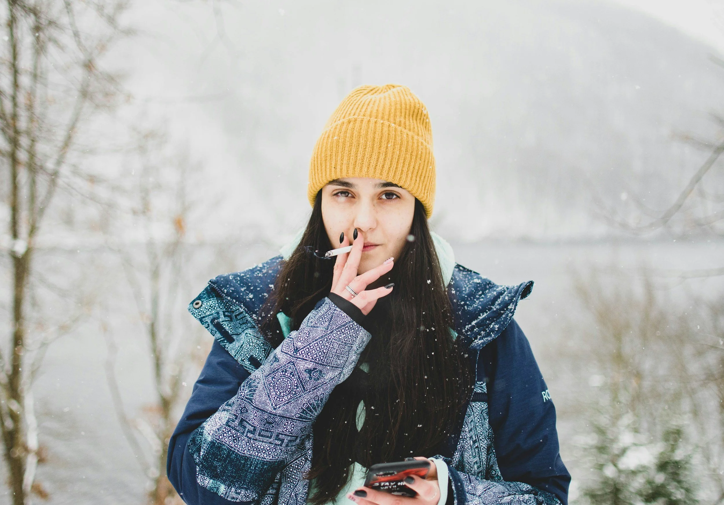 Young woman in a yellow beanie smoking outdoors in falling snow, illustrating the relationship women have with smoking.