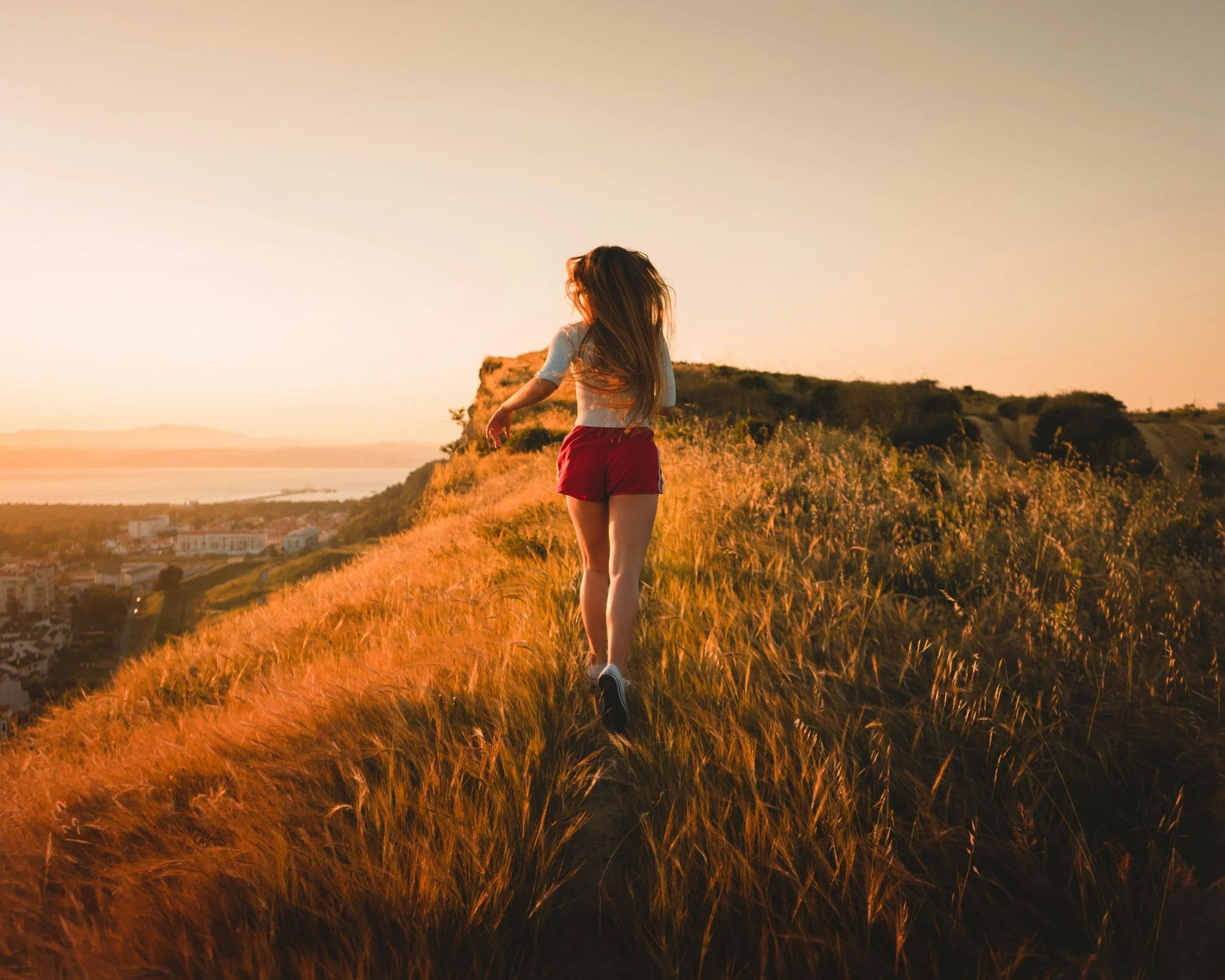 Young woman walking through golden grass at sunset, illustrating the body moving through emotions after quitting smoking.