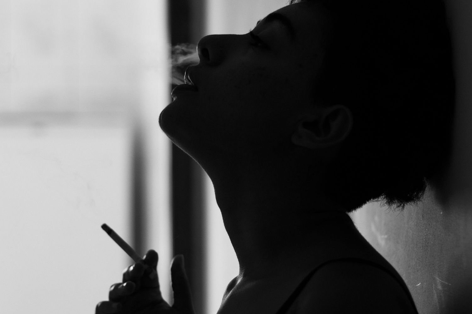 Black and white profile of a woman with her head tilted back and eyes closed, exhaling cigarette smoke illustrating the daily smoking ritual women build their day around