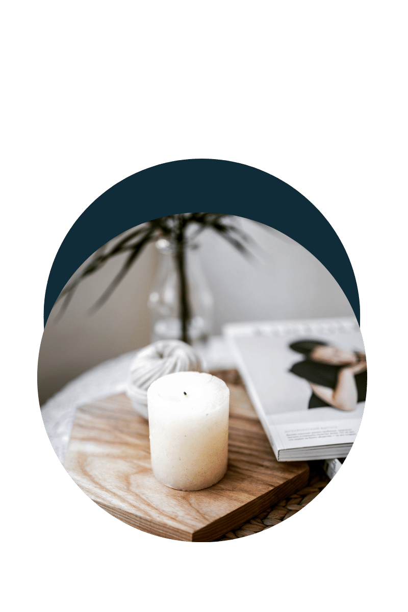 Une bougie blanche sur une planche de bois, avec un magazine ou un livre ouvert à côté, et un vase avec des branches d'une plante verte