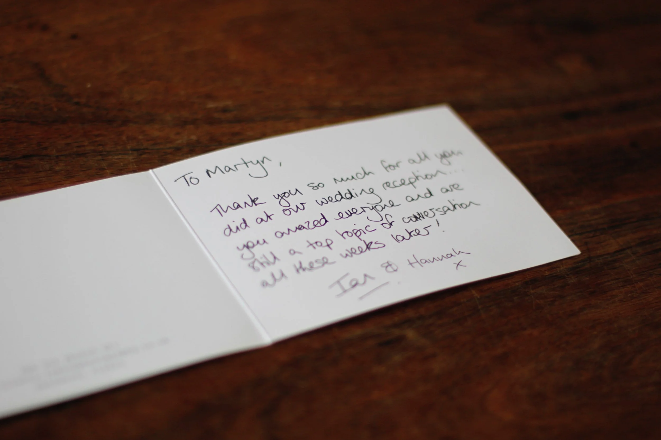 Close-up of a handwritten thank-you note on white paper resting on a dark wooden surface.