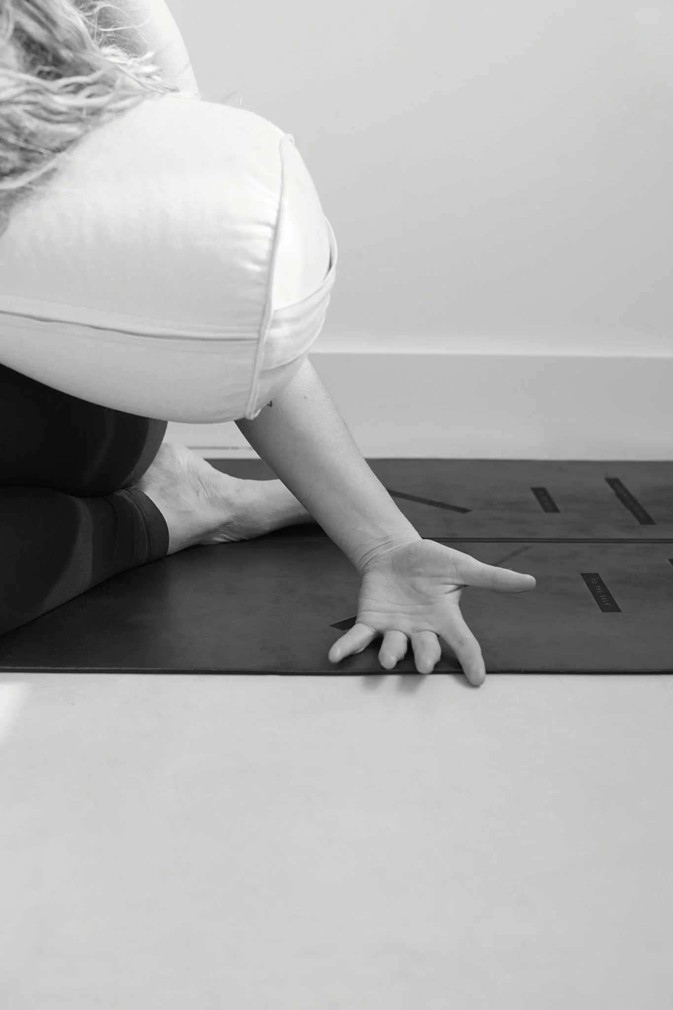 Laura Wilkes practicing yin yoga online on a mat, reaching forward with one arm extended, black and white photograph.