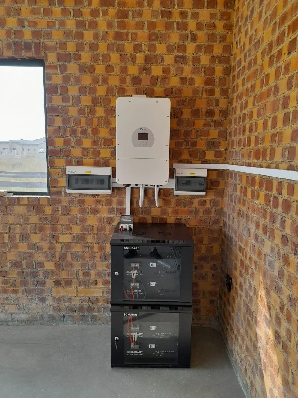 Solar inverters and electrical control panels mounted on a brick wall in a utility room.
