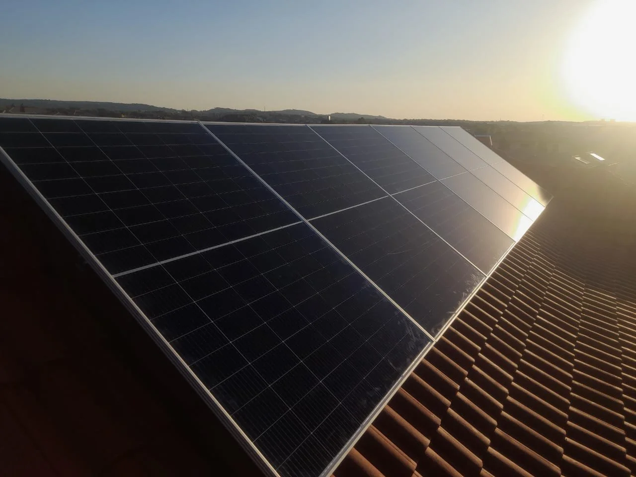 Solar panels installed on a rooftop at sunset with a distant hilly landscape in the background.