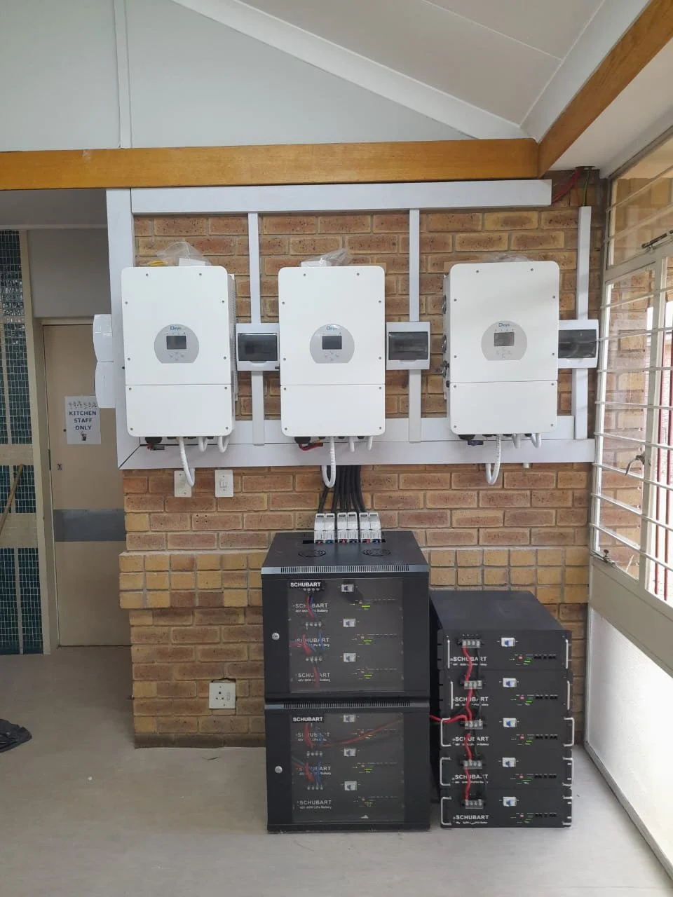 Solar power inverter system with three inverters mounted on a brick wall and connected to power storage units below.