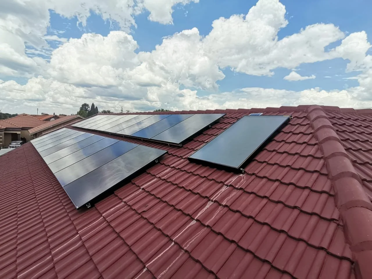 Solar panels installed on a red tiled roof under a partly cloudy sky.