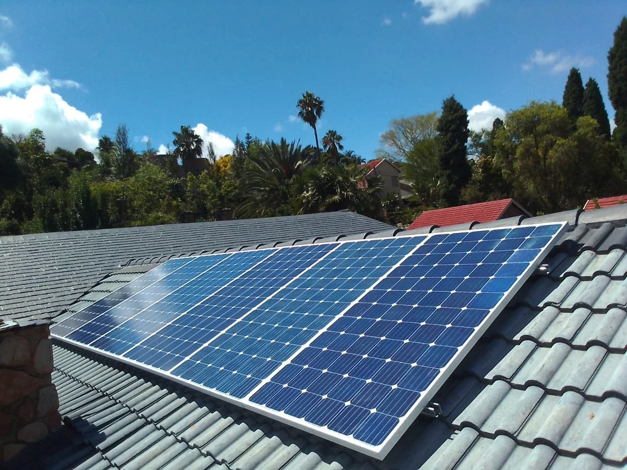 Solar panels installed on a residential rooftop under a blue sky with scattered clouds.
