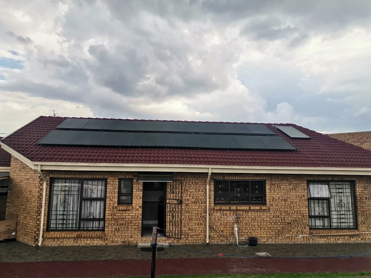 Brick house with solar panels on the roof and stormy clouds overhead.