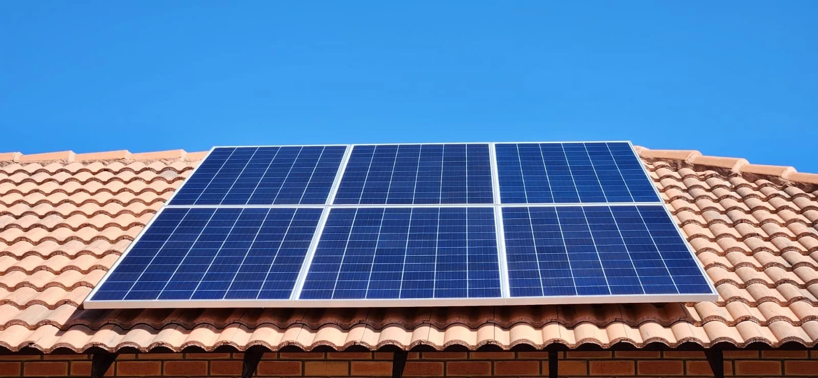 Blue solar panels mounted on a tile roof against a clear blue sky.