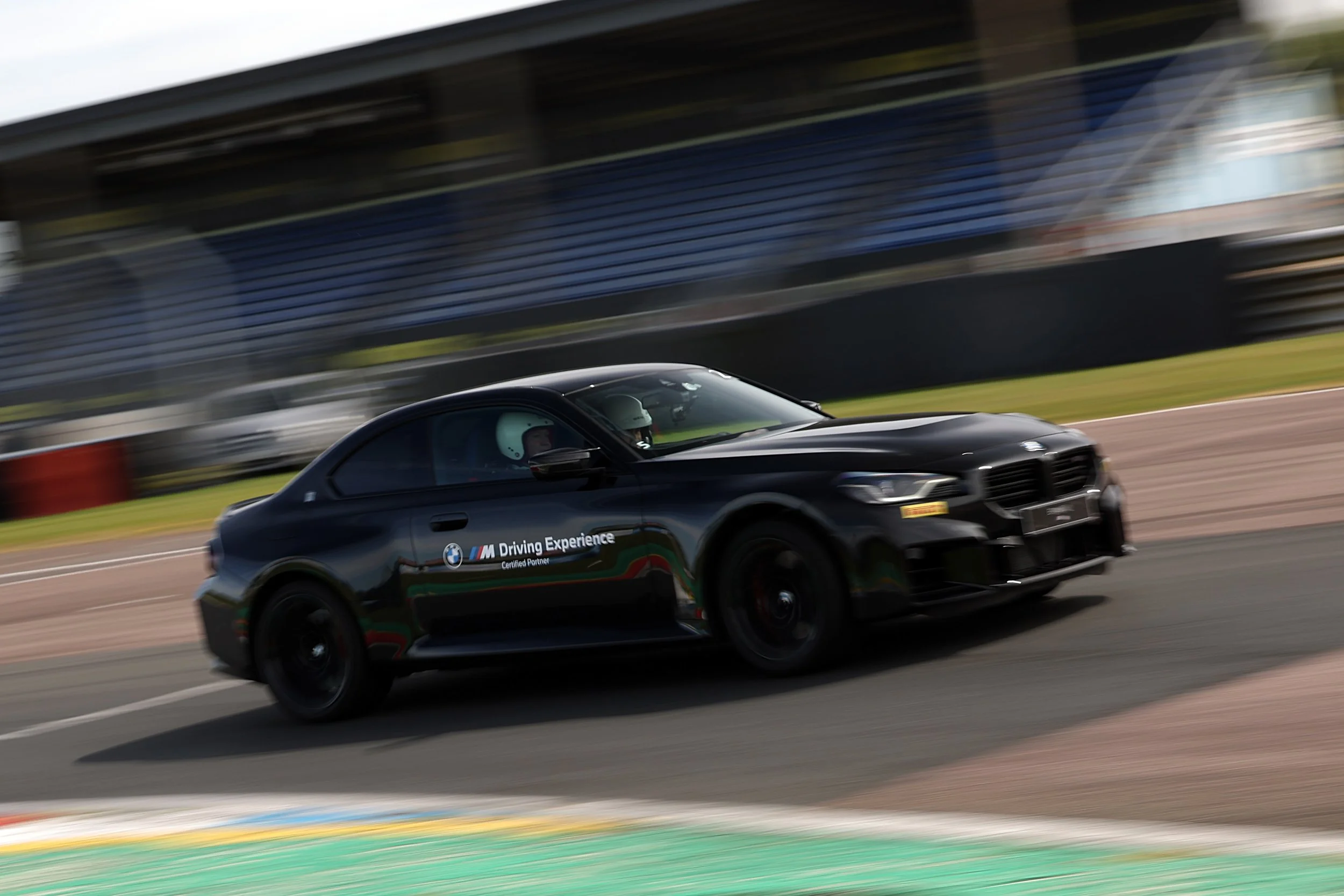 Black BMW racing car with 'M Driving Experience' logo on side, speeding on a race track with blurred background.