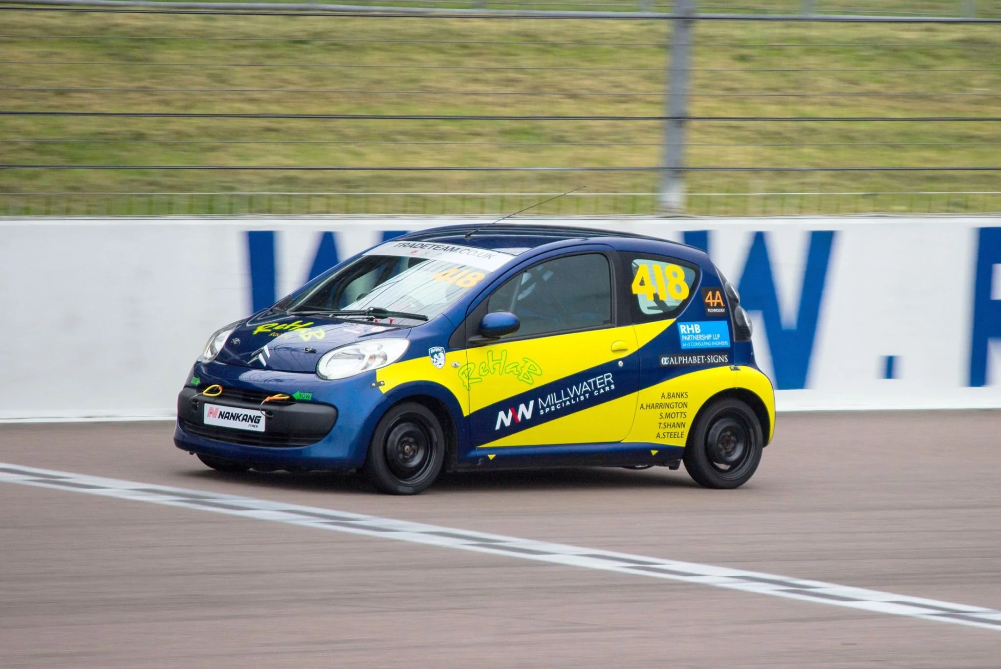 A small blue and yellow race car on a racetrack with sponsor logos and the number 418.