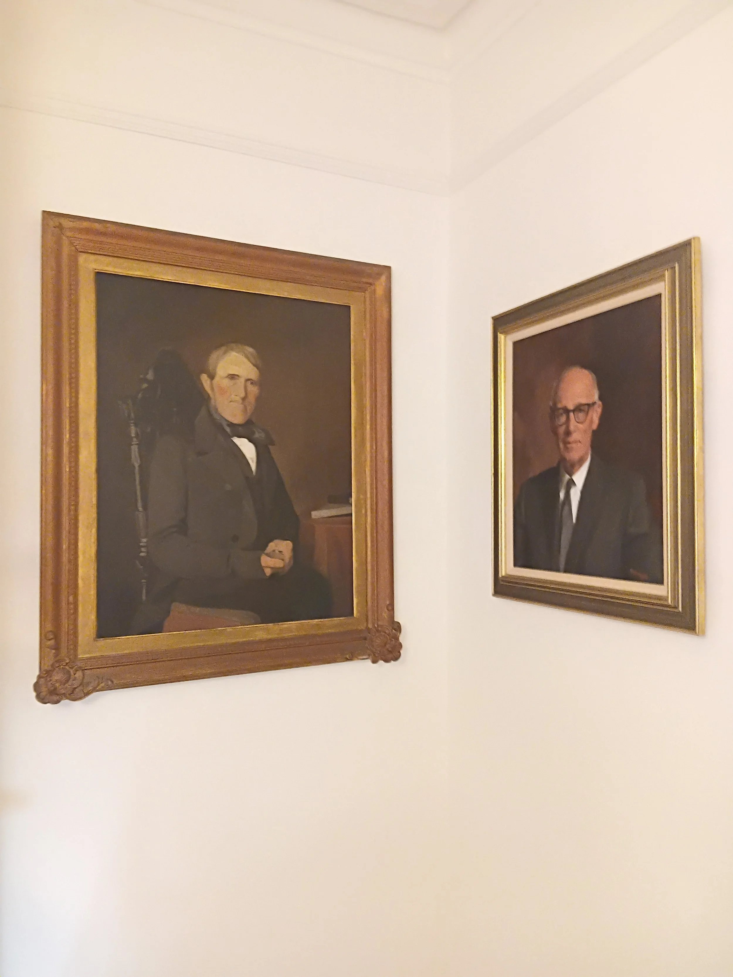 Two framed portraits of men hanging on a white wall.