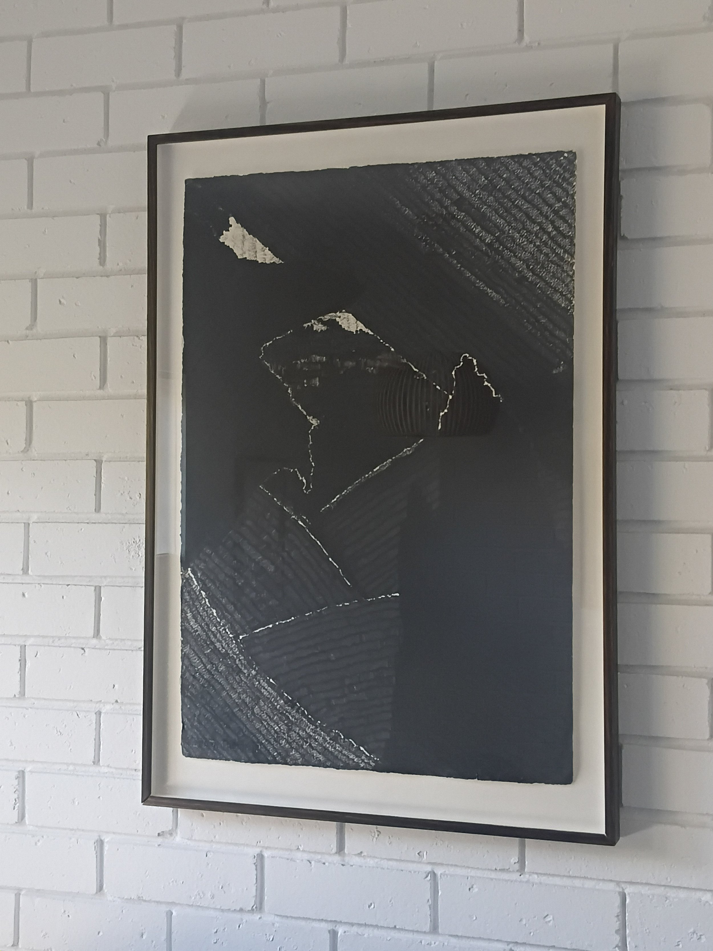 Black and white abstract artwork framed and hung on a white brick wall.