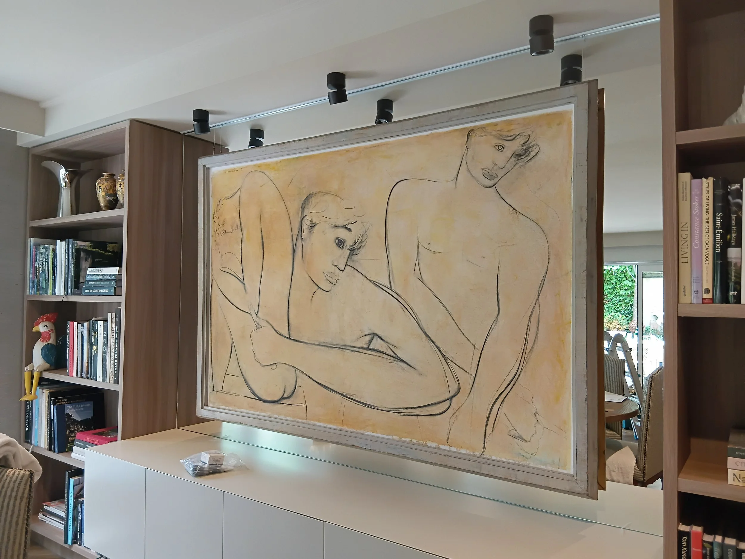 A large painting of two women, one with short hair and the other with long hair, in a minimalist style with black outlines, displayed on a room divider.