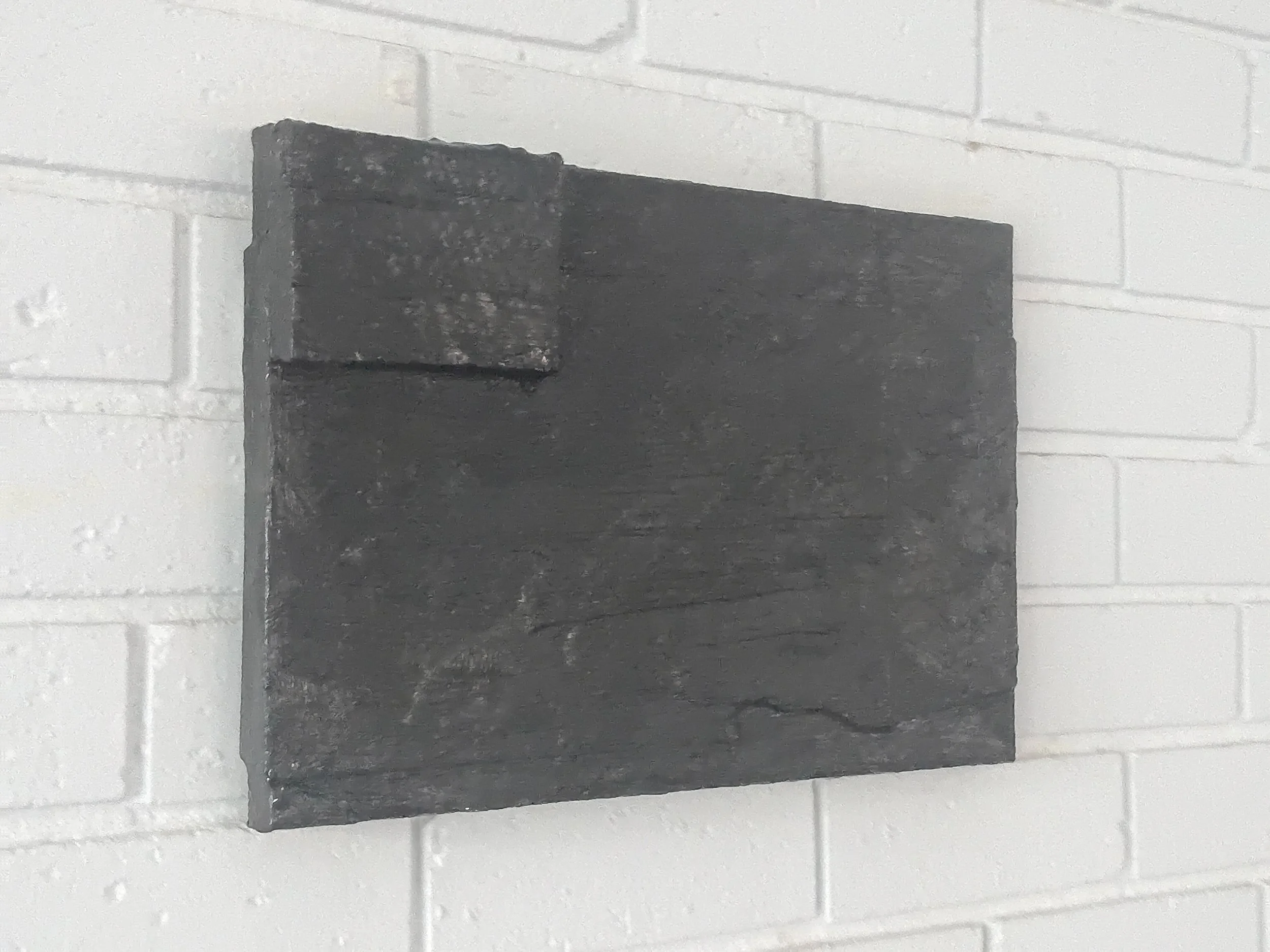 A black rectangular object mounted on a white brick wall.