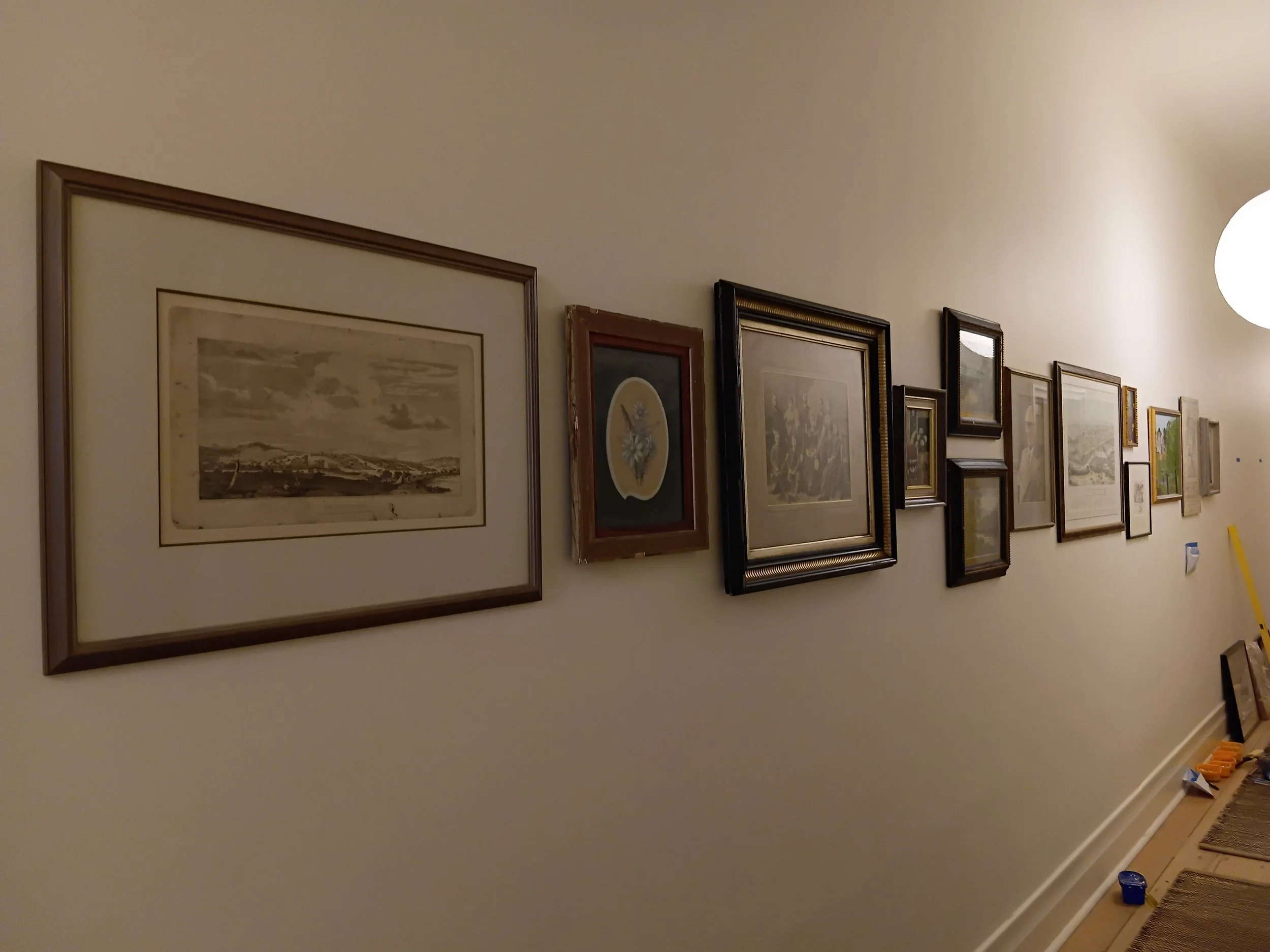 A gallery wall with framed artwork hanging on a beige wall in a home or gallery setting.