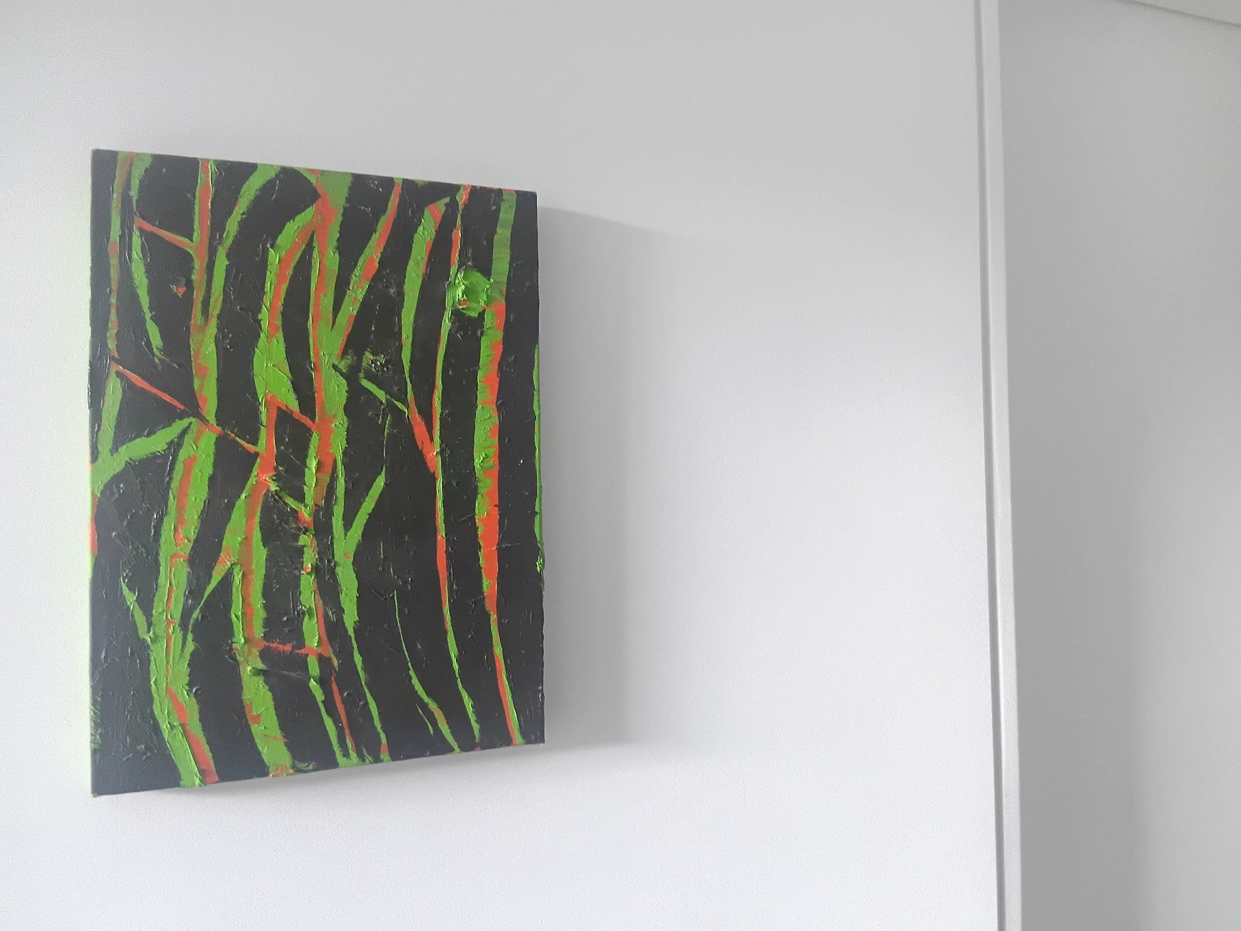 Abstract painting with black background and bold green and orange diagonal lines, hung on a white wall.