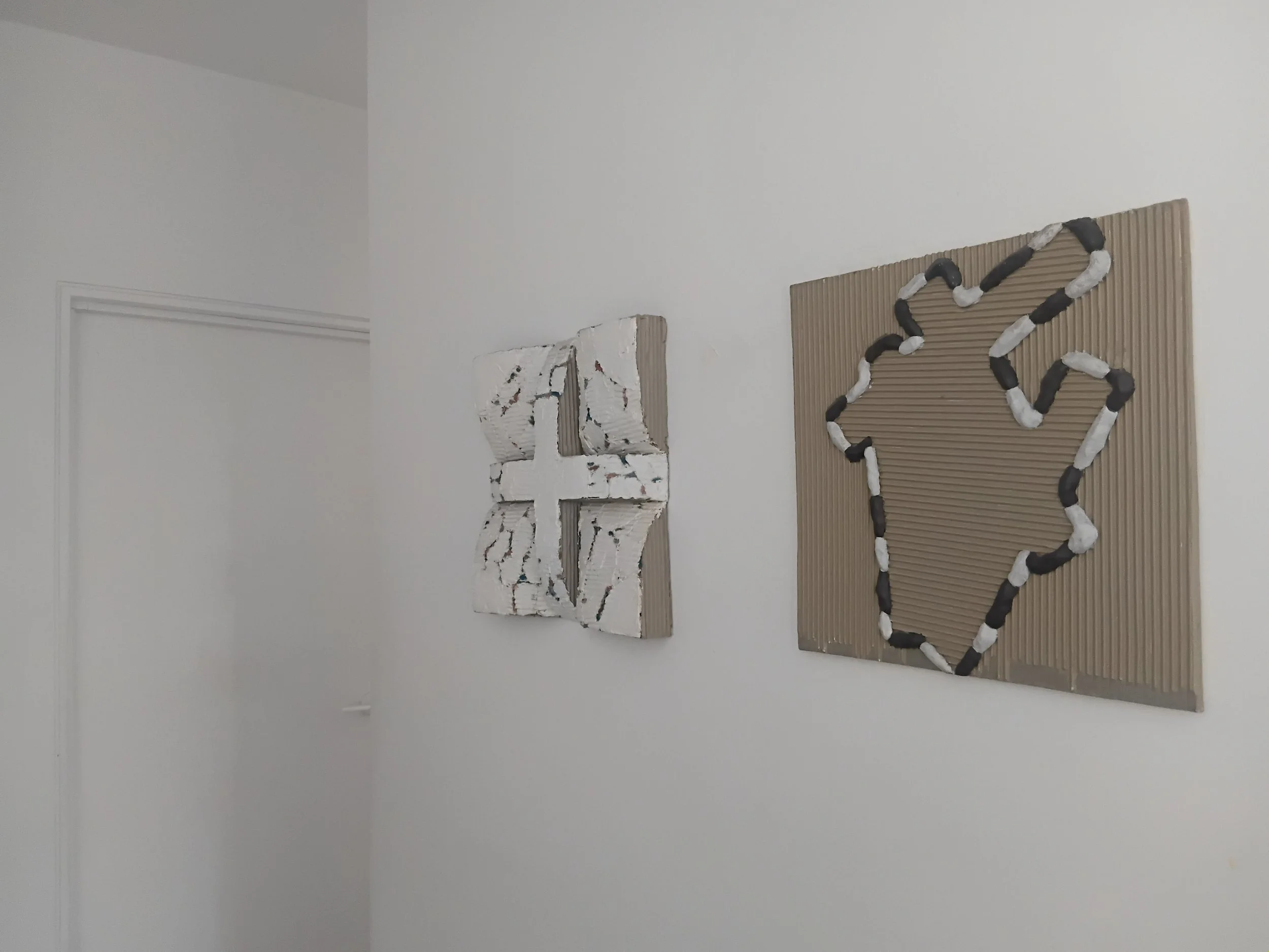 A wall with decorative items, including a large felt number '23' made of black and white connected pieces on a ribbed brown panel, and a white textured abstract art piece with rough, uneven surfaces.