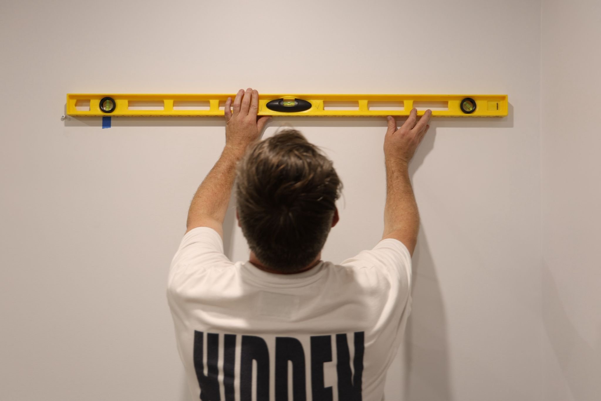 Person using a yellow spirit level on a white wall.