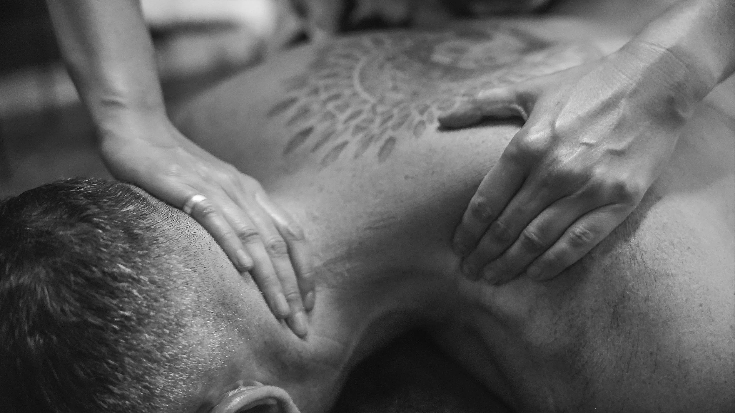 Close-up of a person receiving a massage, focusing on the back with hands applying pressure on the shoulders and upper back.