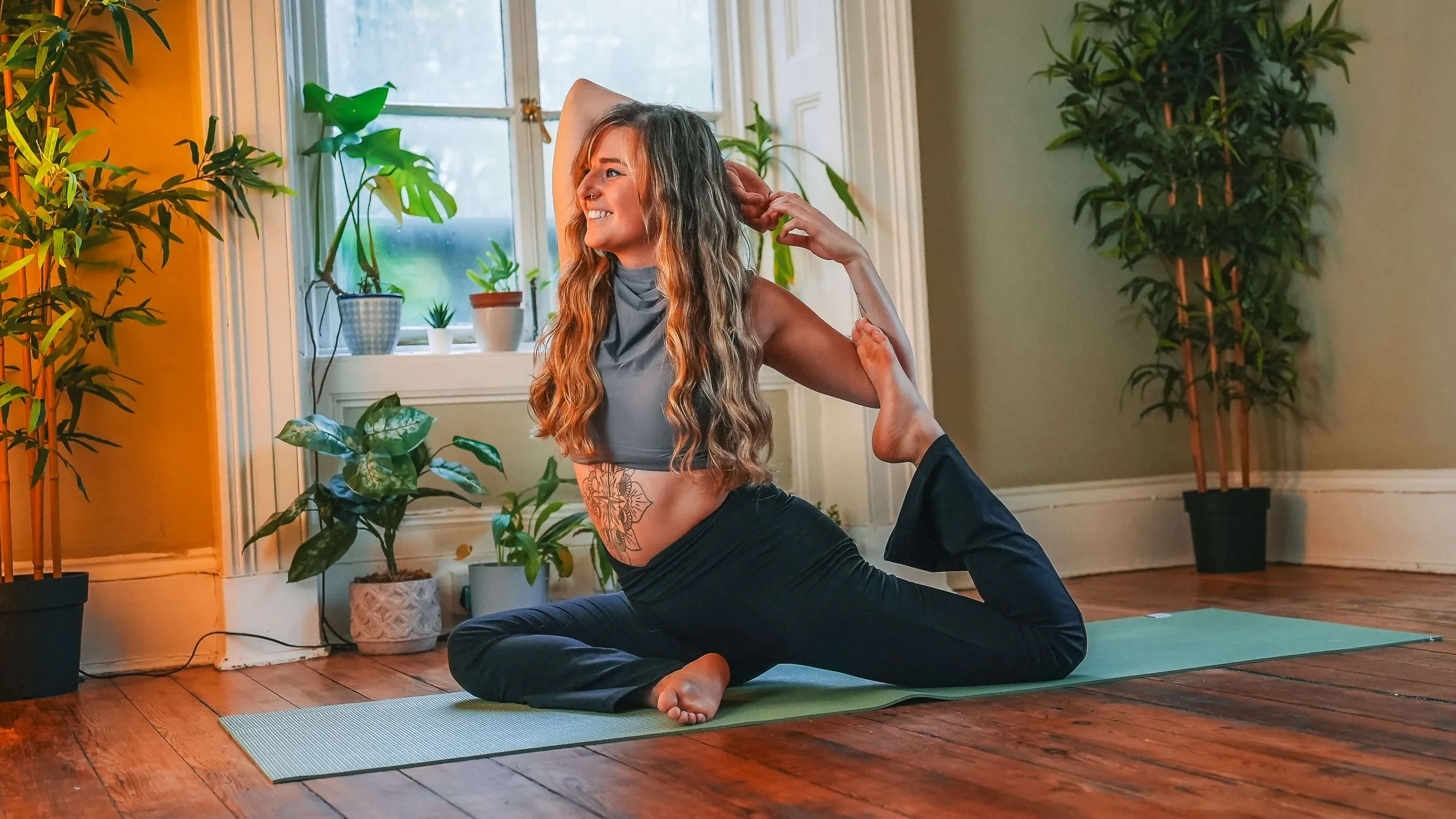 Woman practicing yoga in a sunlit room with green plants and wooden floors.