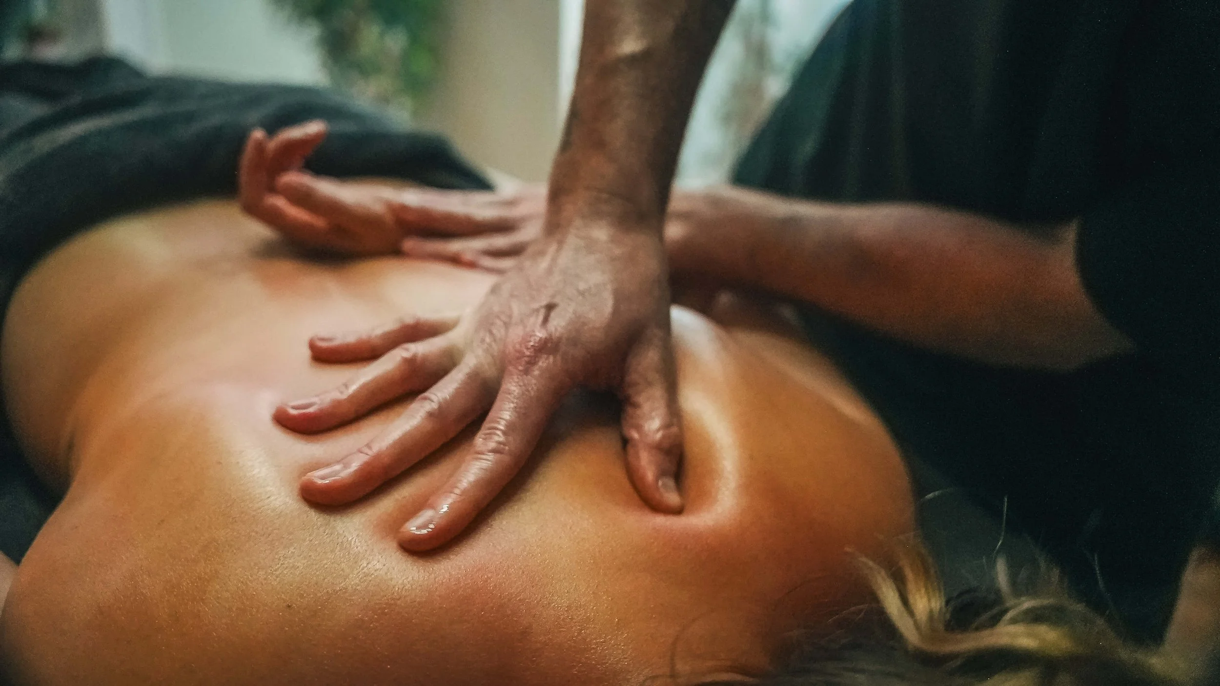 A person receiving a massage in a spa setting, lying face down with hands massaging their back.