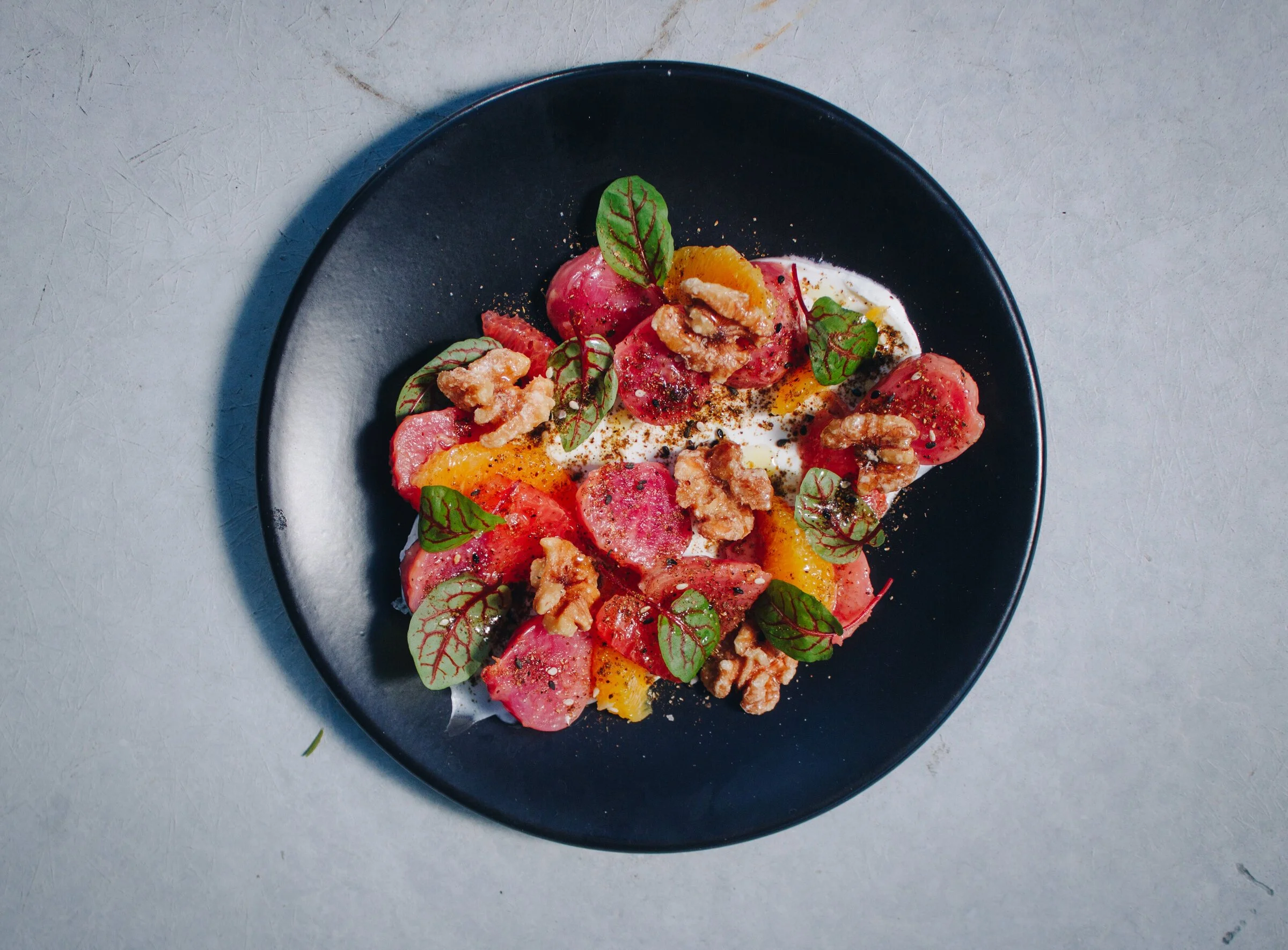 Salad with radish slices, orange pieces, walnuts, green leaves, and a creamy dressing on a black plate.