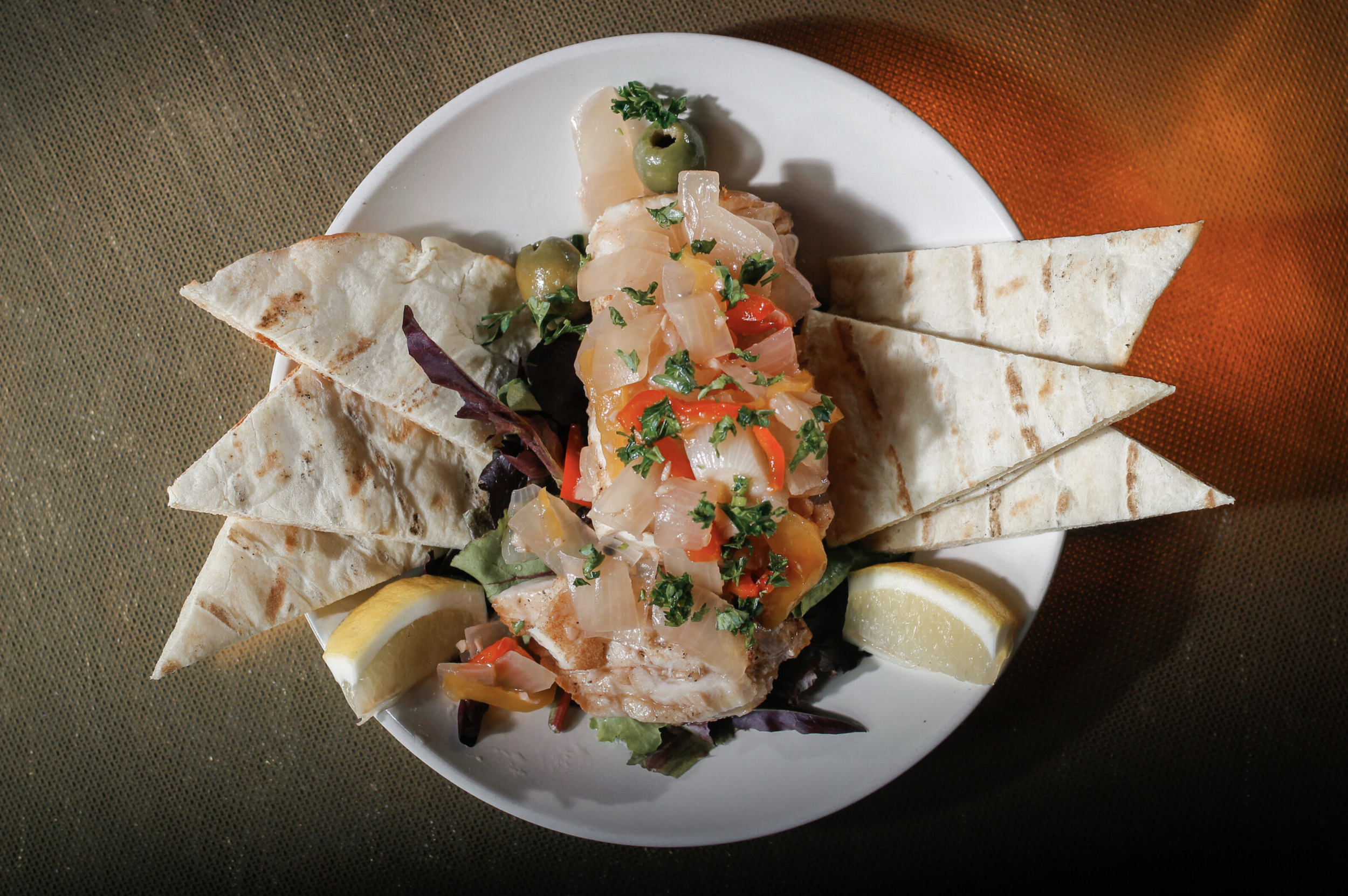 A plate of fish served with pico de gallo, lemon wedges, chips, and olives on the side.