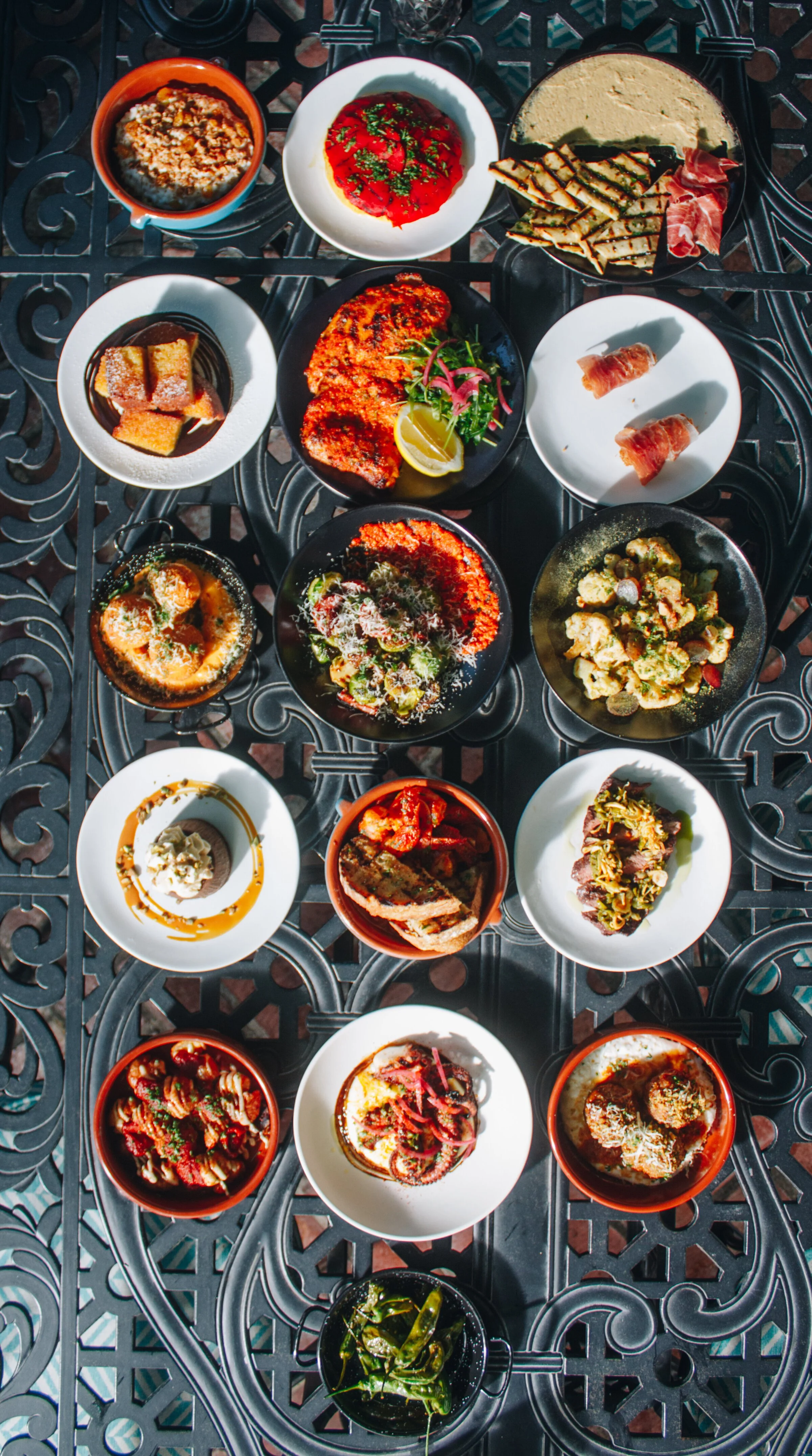 Assorted Italian dishes on a metal table, including pasta, salads, grilled vegetables, and cured meats.