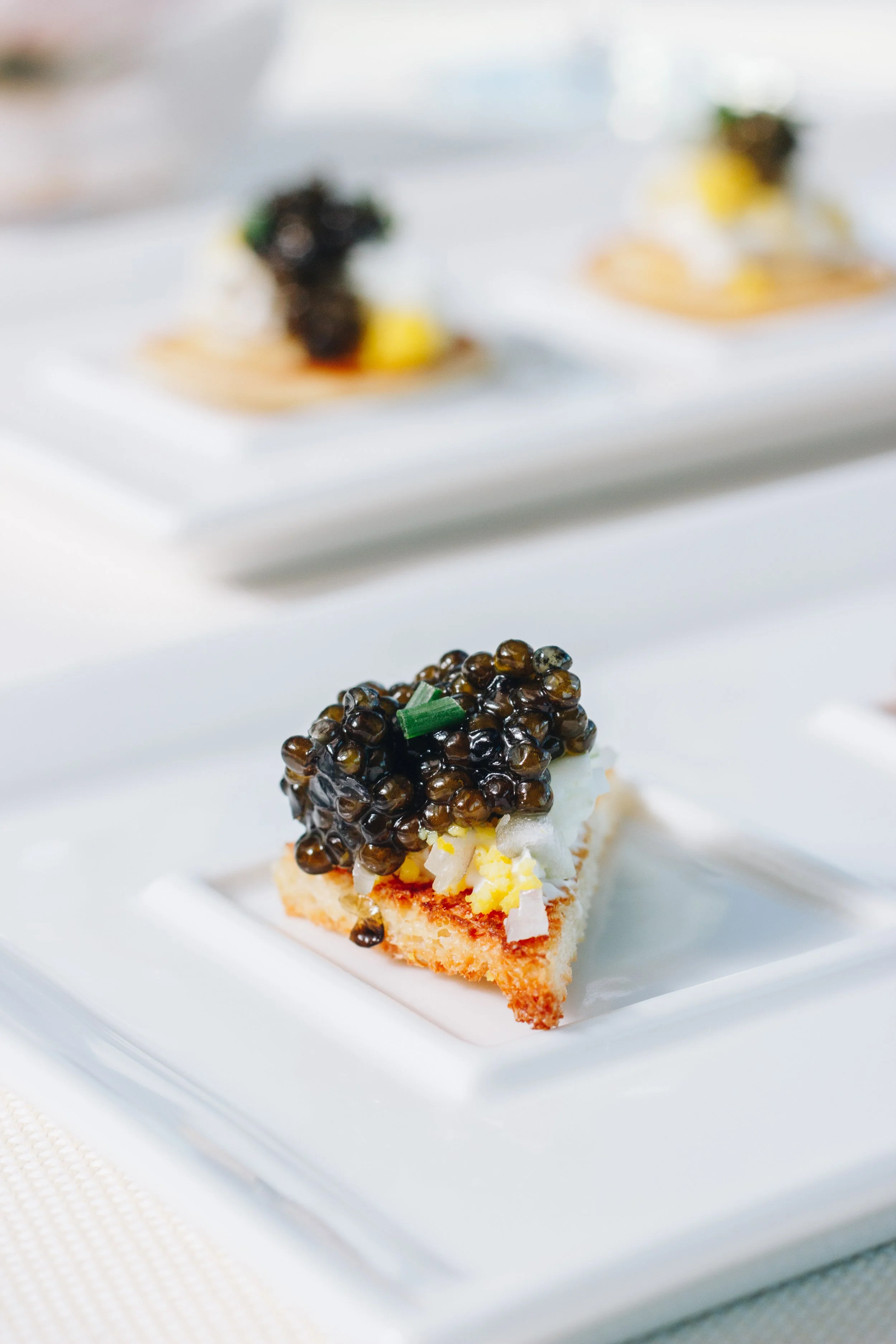 Close-up of a canapé with black caviar and chopped egg on a small piece of bread.