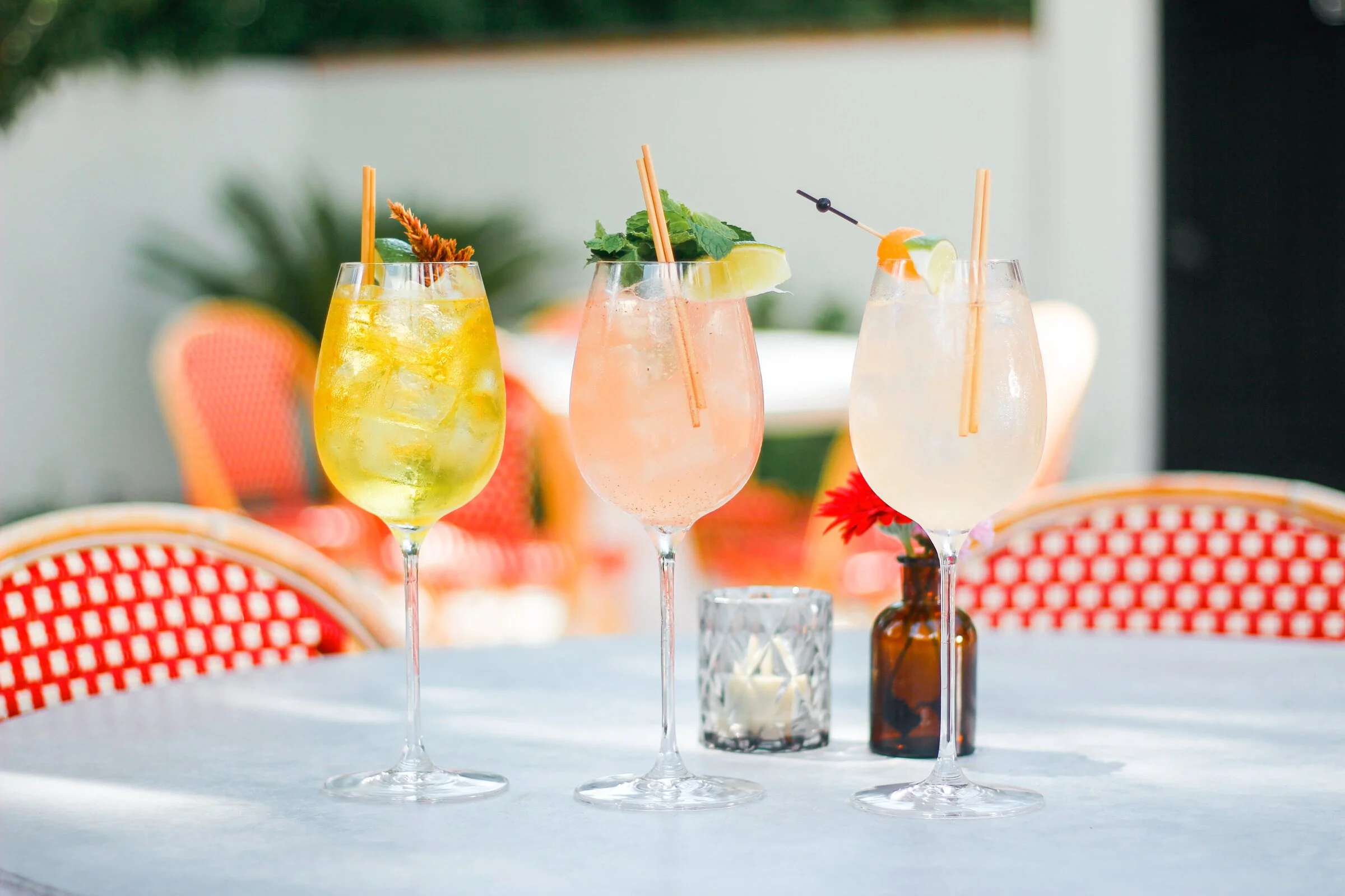 Three colorful cocktails on a table decorated with flowers and candles.