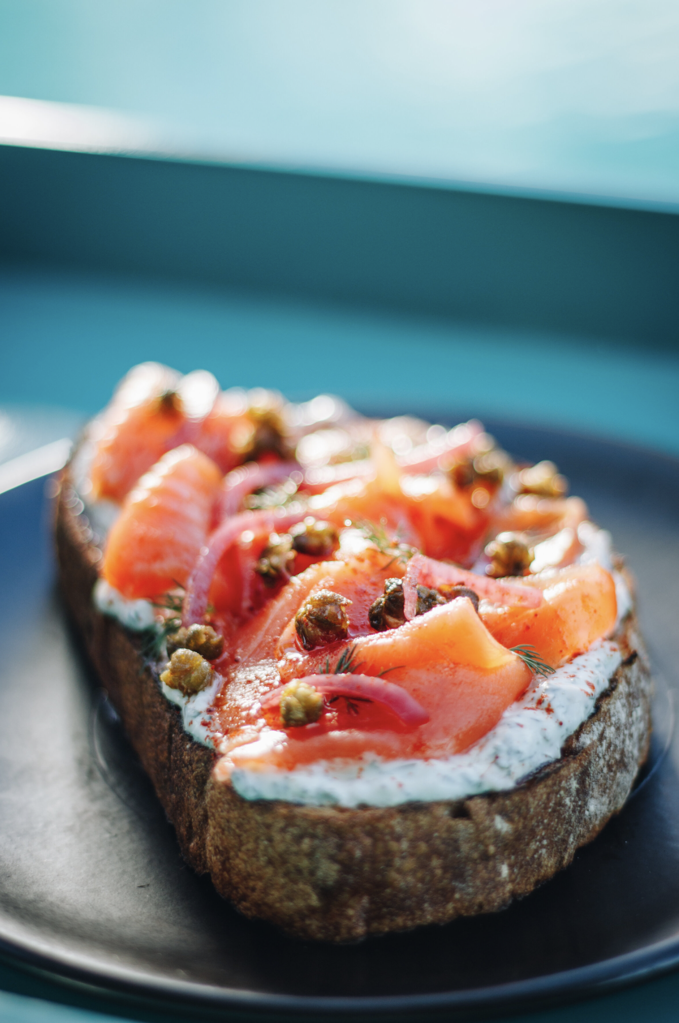 An open-faced bagel sandwich topped with smoked salmon, red onion slices, capers, and dill on a black plate.