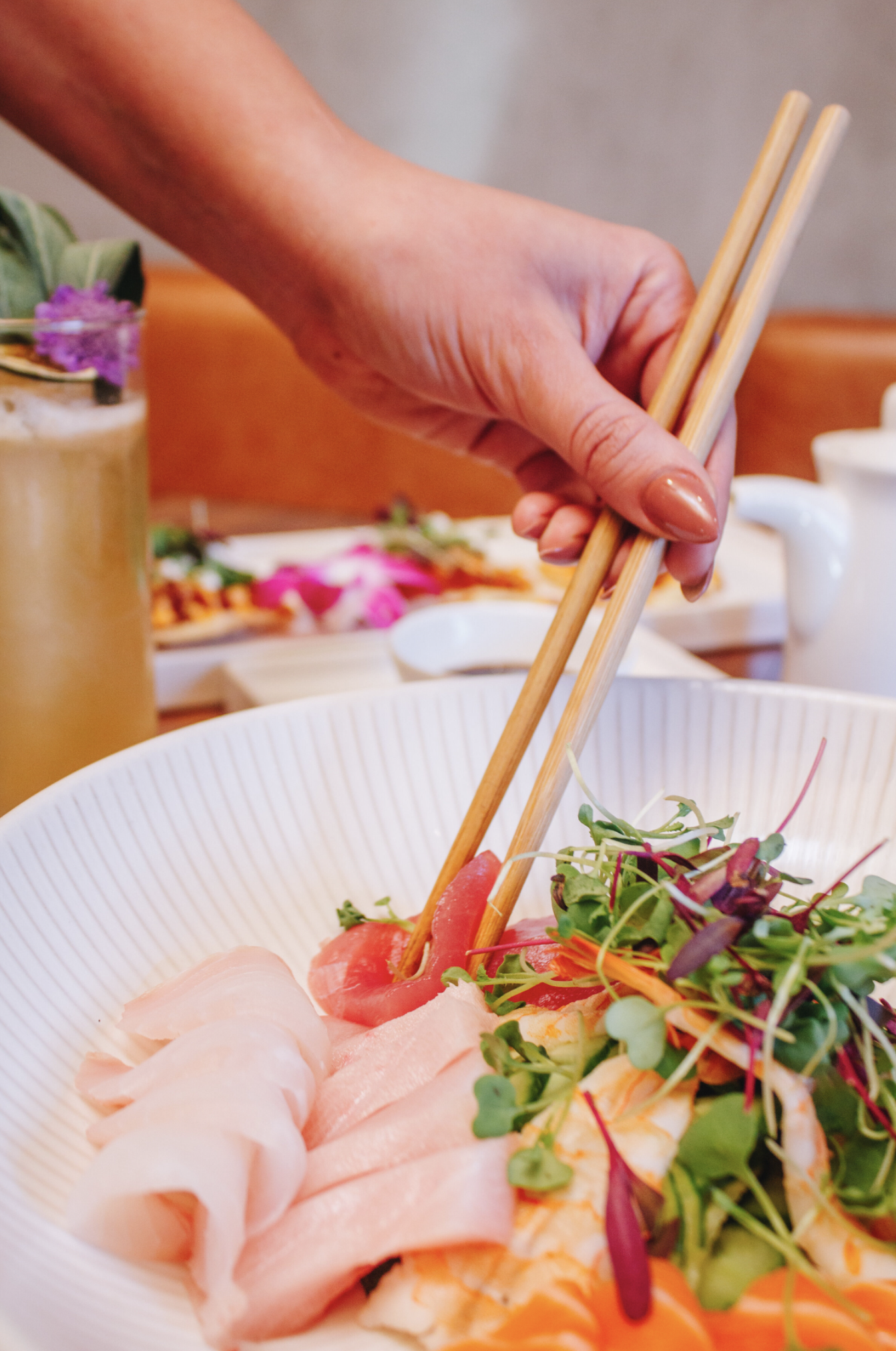 Person using chopsticks to pick up sashimi and salad in a white bowl at a restaurant.