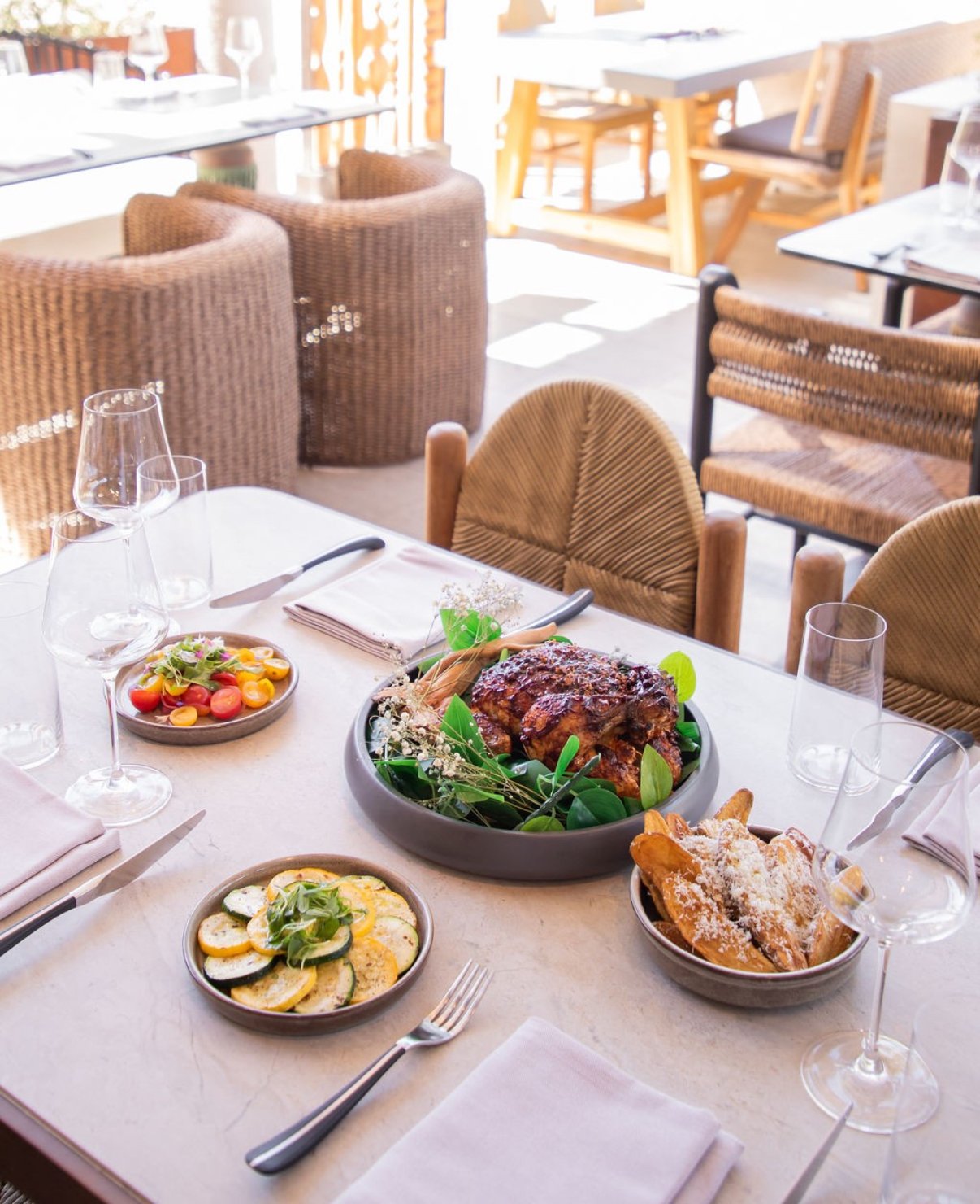 Table set with a roasted meat, salads, bread, and wine glasses in a bright restaurant.