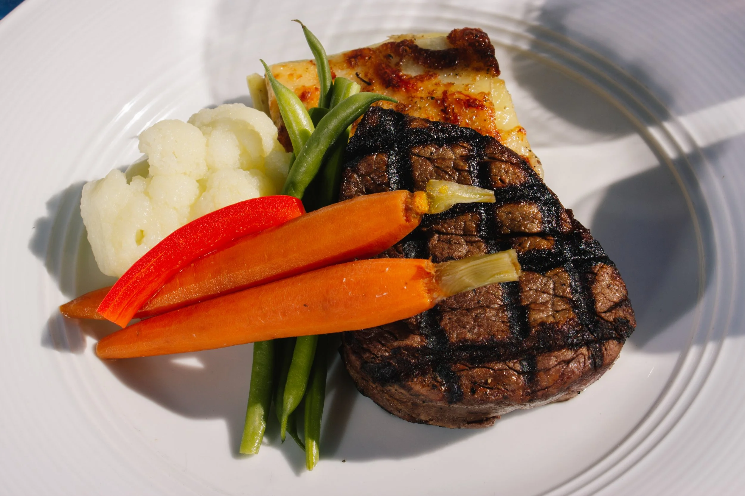 Grilled steak with vegetables, mashed potatoes, and cauliflower on a white plate.