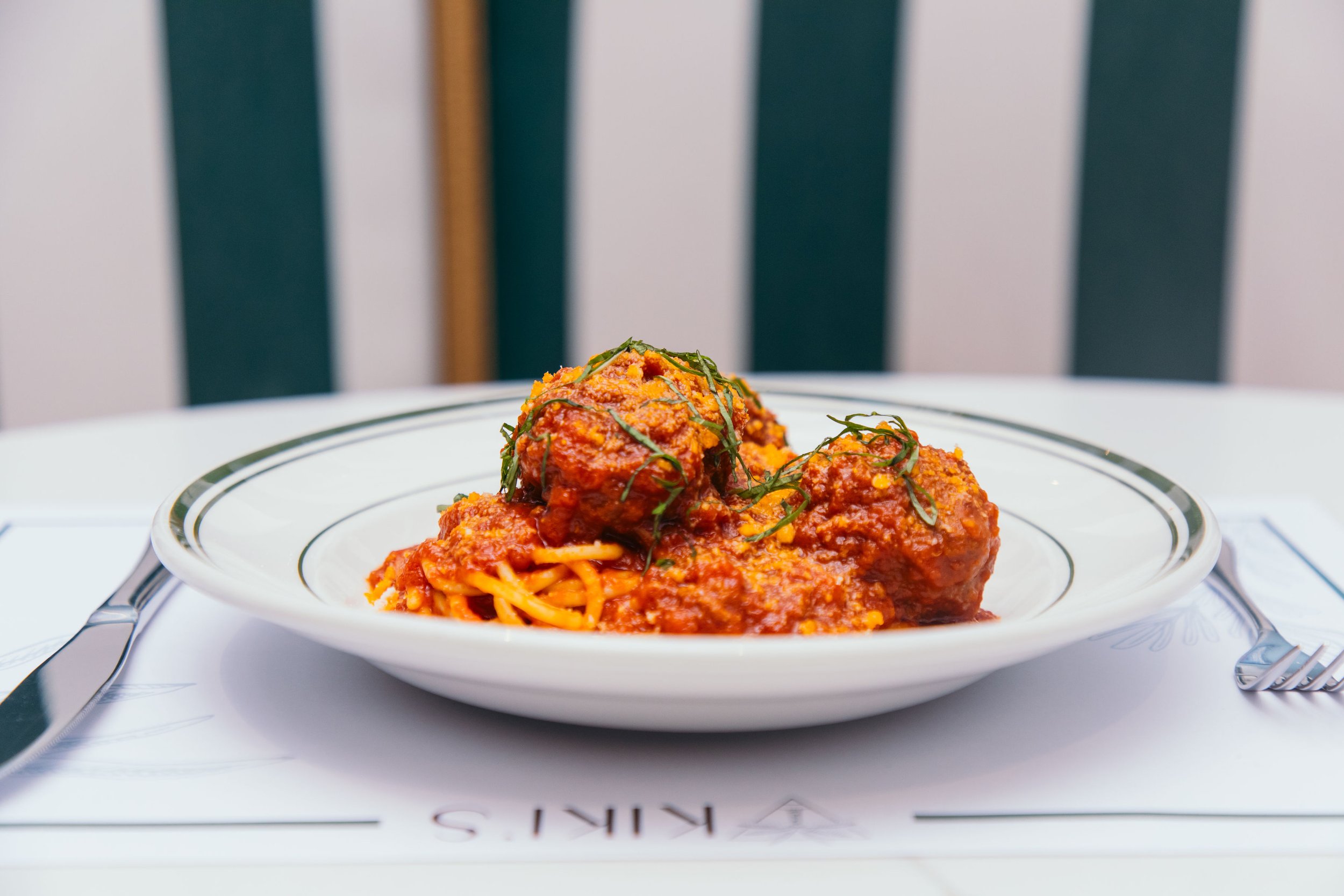 Plate of spaghetti with meatballs in tomato sauce, garnished with herbs on a white table setting.