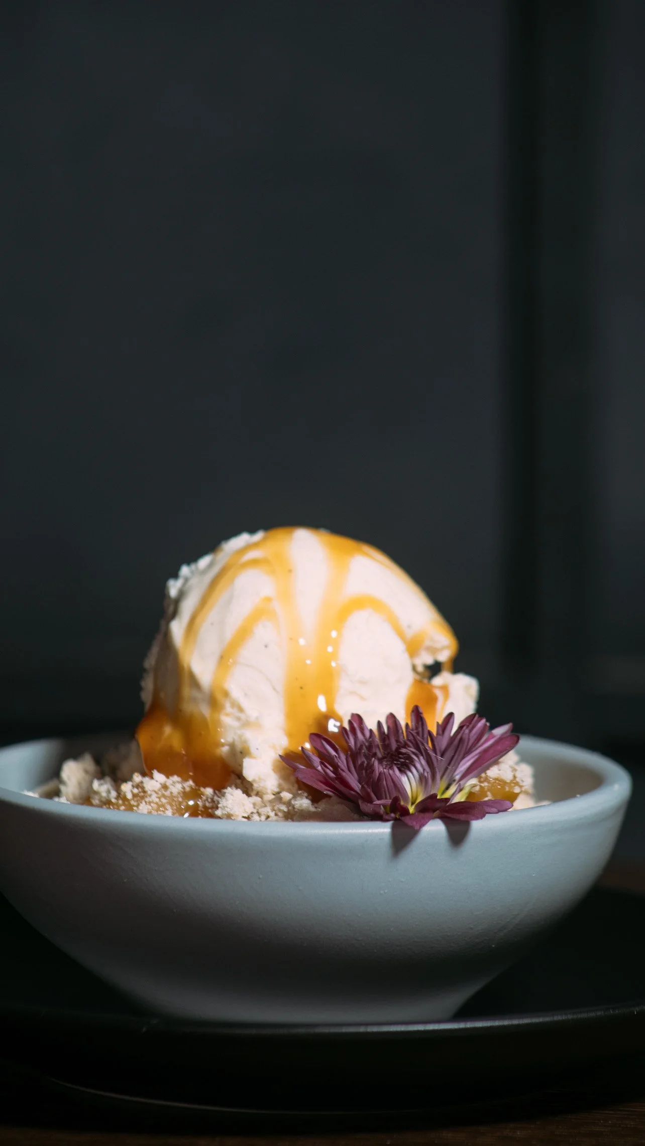 Vanilla ice cream topped with caramel sauce, served in a white bowl with a decorative flower.