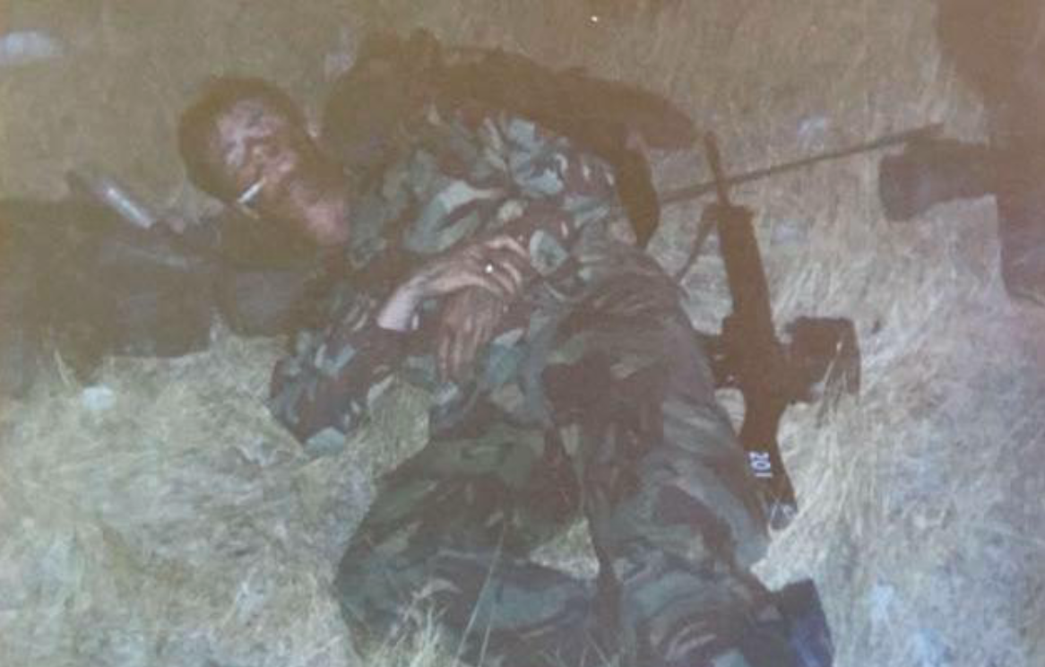 Soldier in camouflage uniform lying on the ground with a rifle, in a field.