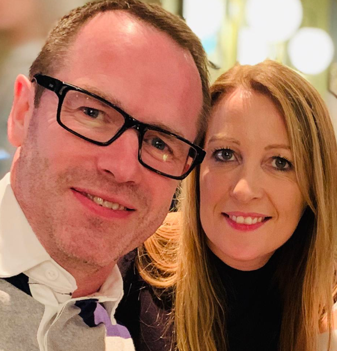 Close-up of a man with glasses and a woman smiling, both looking at the camera.