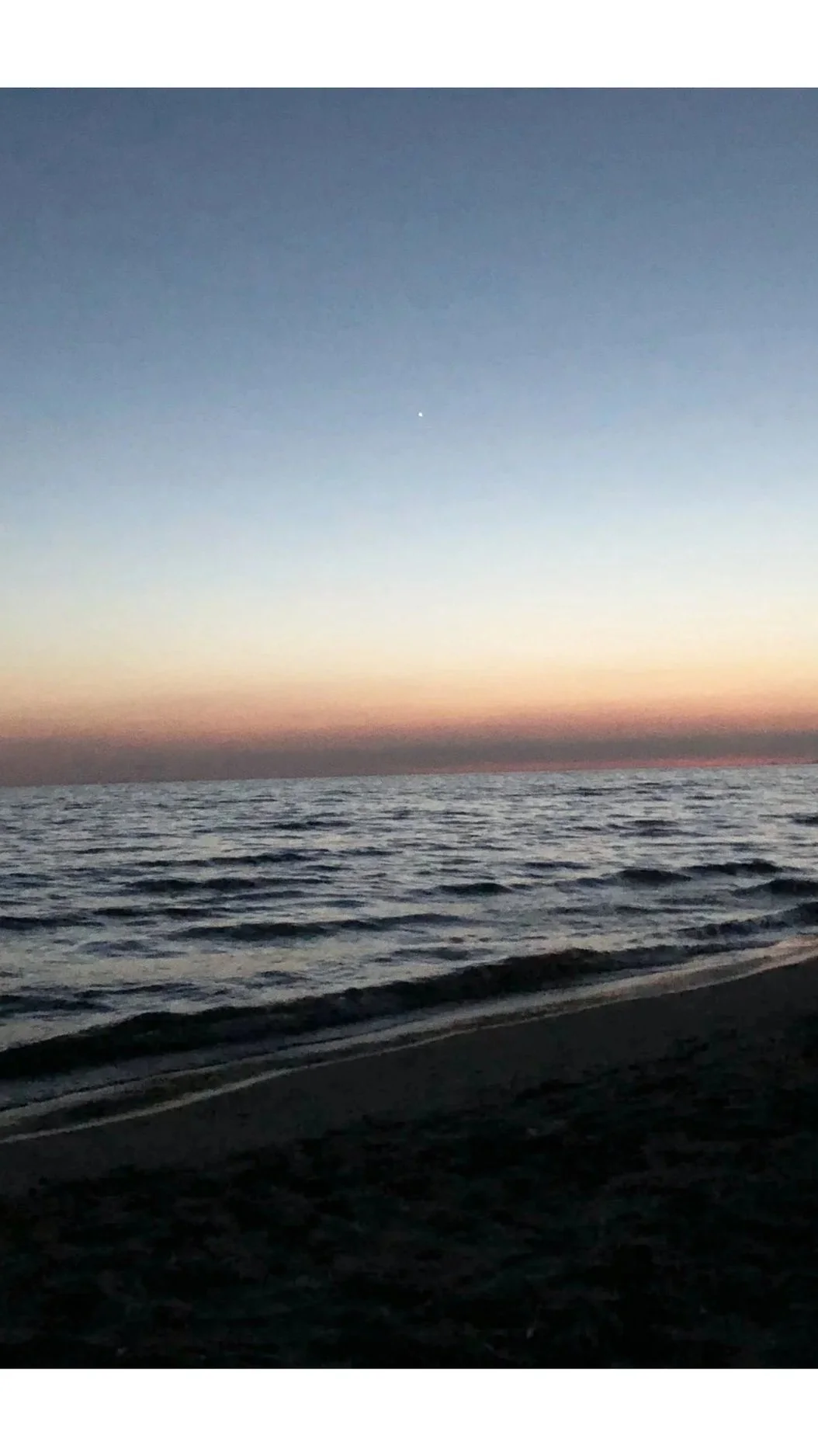Sunset over the ocean with a pastel sky and calm waves, view from the beach.