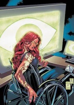 A woman with pink hair and glasses sitting in a wheelchair, smiling, surrounded by computer monitors and electronic equipment.
