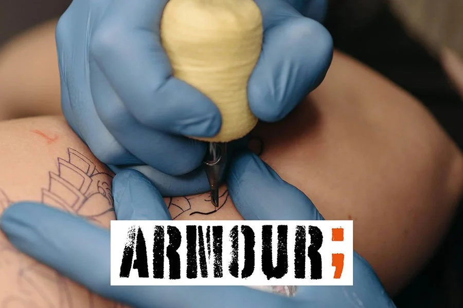 Close-up of a person getting a tattoo, with a tattoo machine held by a gloved hand, in progress on the person's arm.