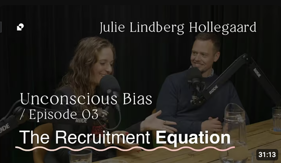 To personer taler i en podcast-opsætning med mikrofoner, og teksten på billedet er 'Julie Lindberg Hollegaard, Unconscious Bias, Episode 03, The Recruitment Equation'.